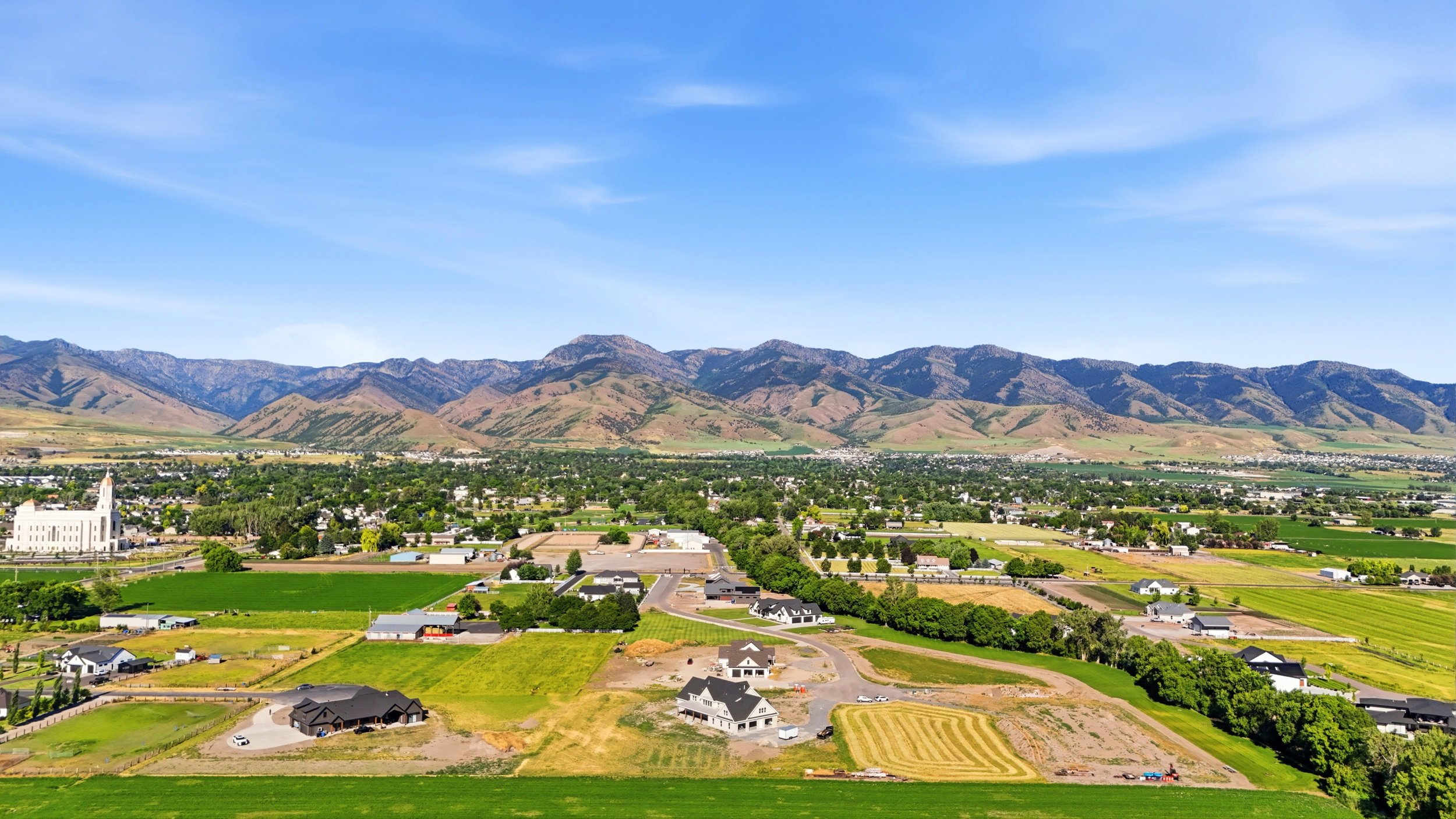 Expansive aerial landscape featuring a large community with developing residential areas, surrounded by green agricultural fields
