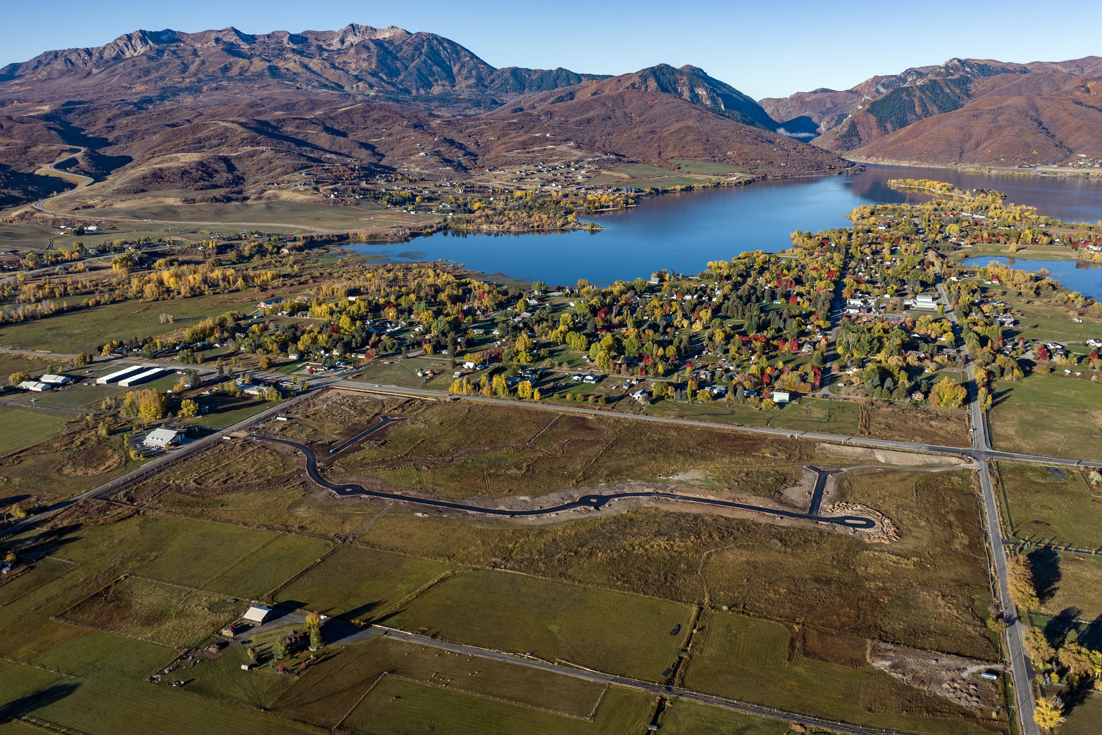 Expansive land parcel featuring a newly paved road, surrounded by agricultural fields and distant mountainous terrain