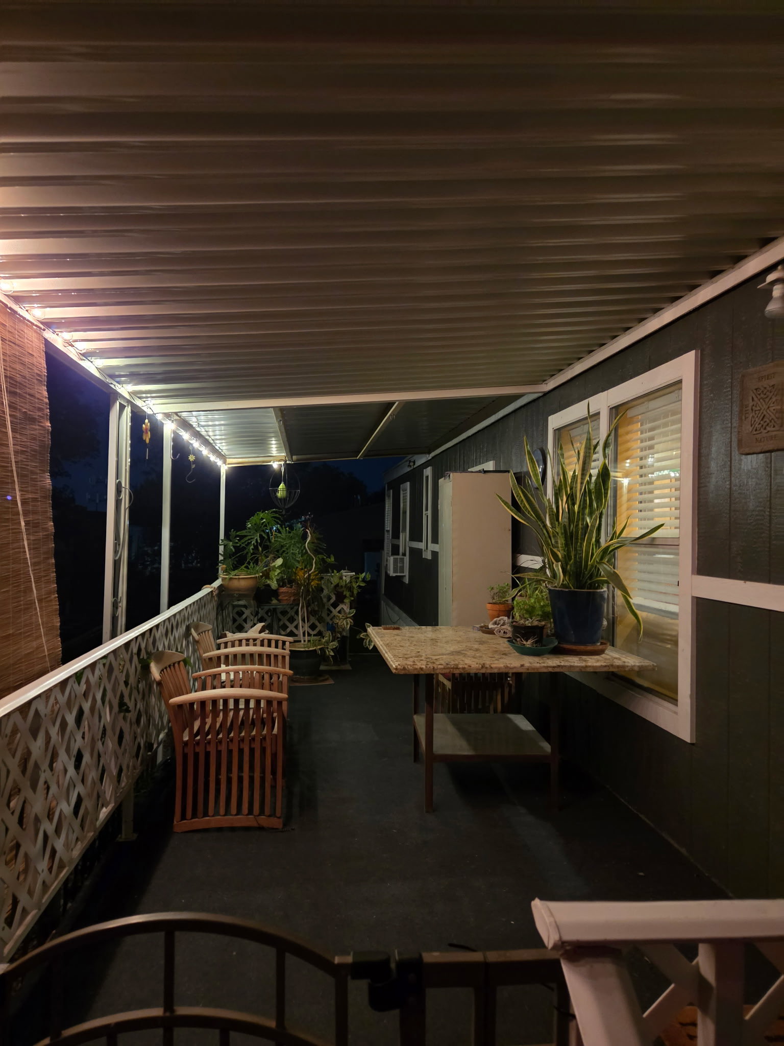Expansive covered patio featuring a dark-toned floor, white lattice railing, and a white corrugated ceiling