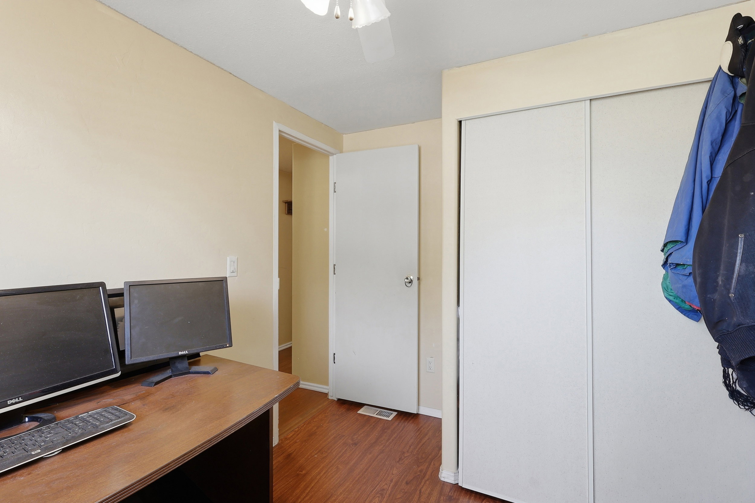 Room featuring wood-finish flooring, light-toned walls, a white ceiling fan, and white bi-fold closet doors