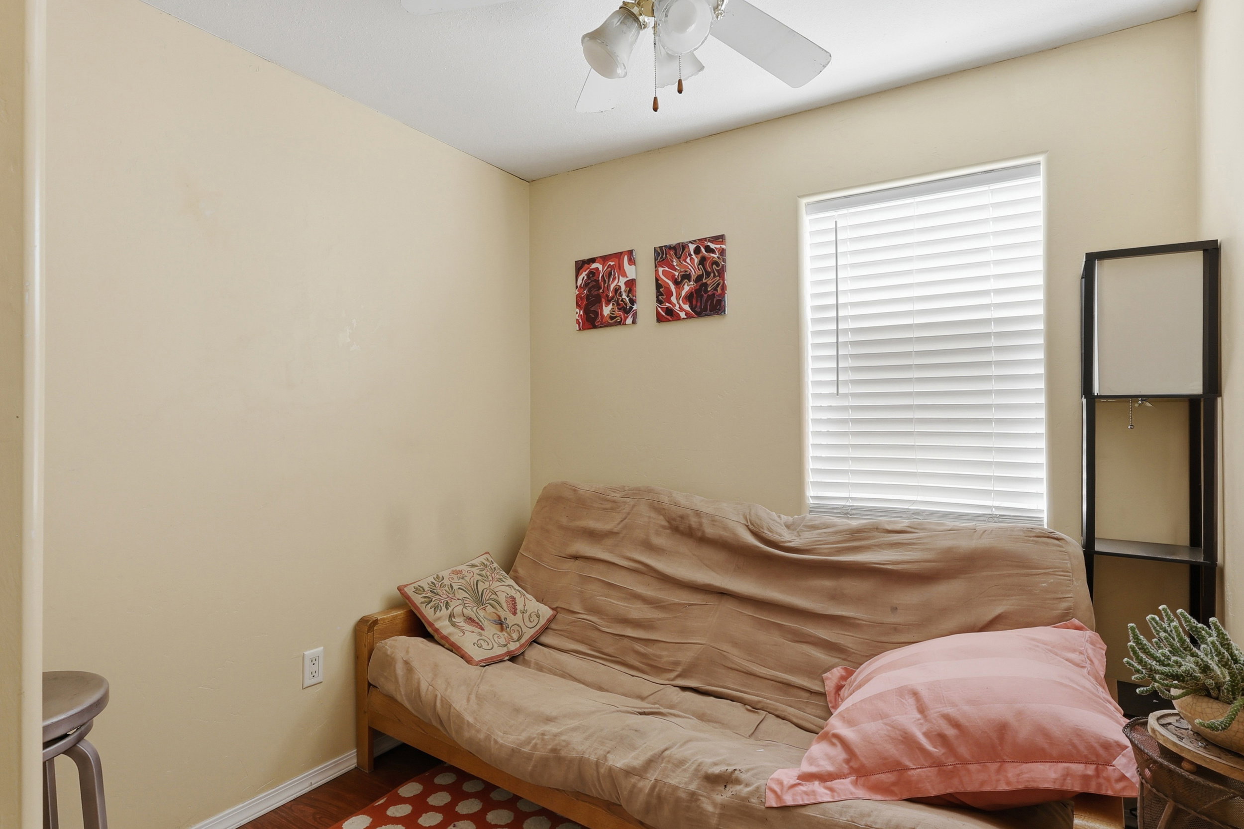 Compact room featuring a window with horizontal blinds, wood-finish flooring, a ceiling fan, and neutral-toned walls