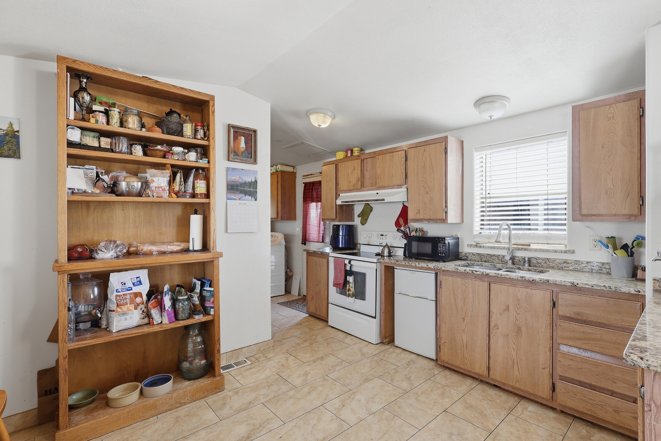 Kitchen featuring tile flooring, light wood-finish cabinetry, a window with blinds, and white appliances