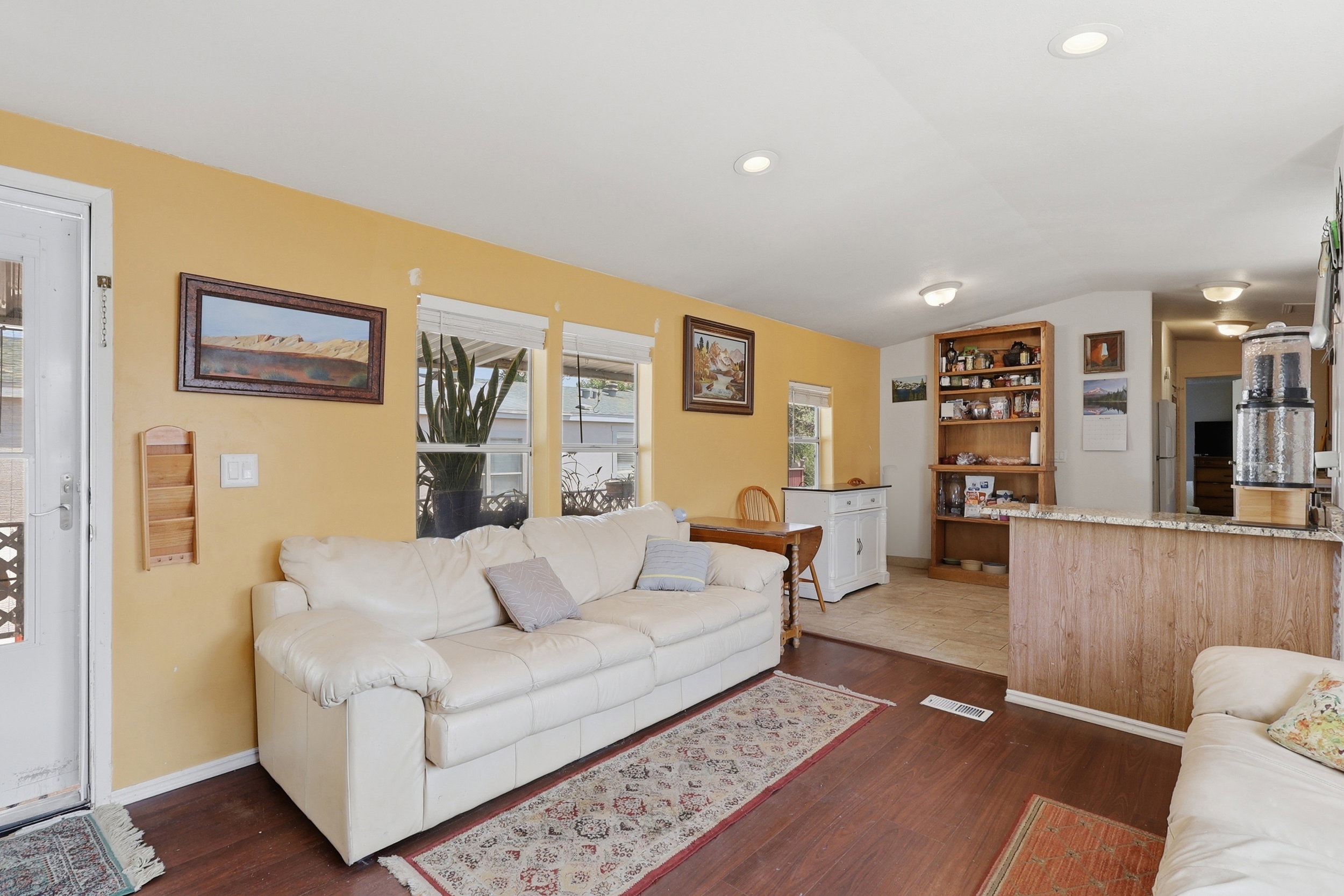Open-concept living area featuring wood-finish flooring, multiple windows providing natural light, and a breakfast bar with a stone-look countertop