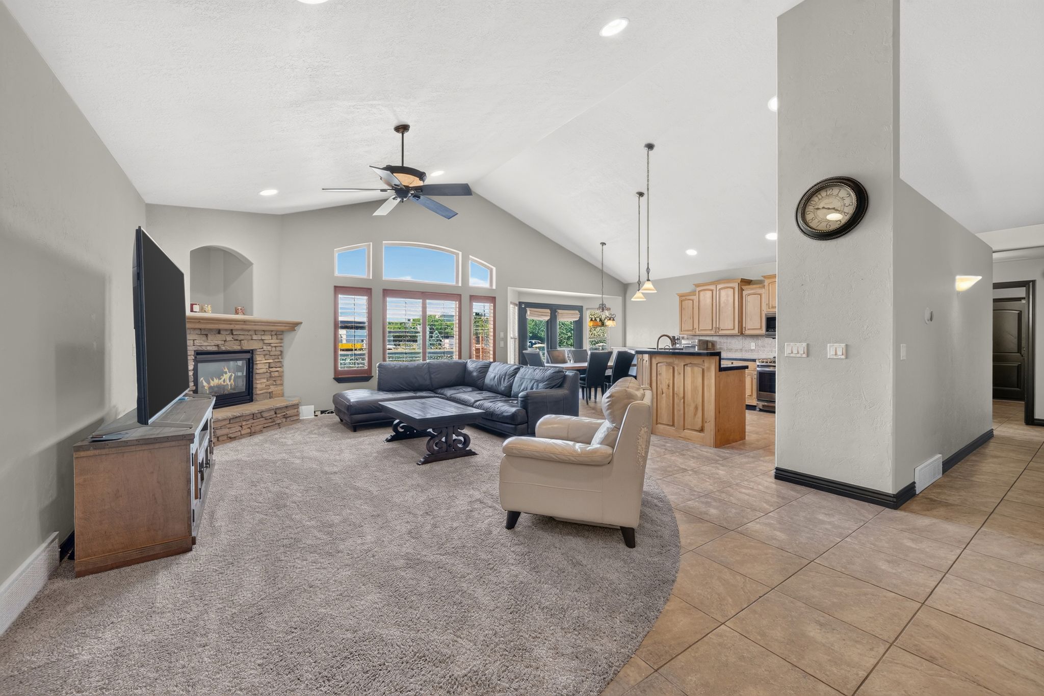 Vaulted ceiling living area featuring a stone-faced fireplace, large windows, recessed lighting, and a ceiling fan