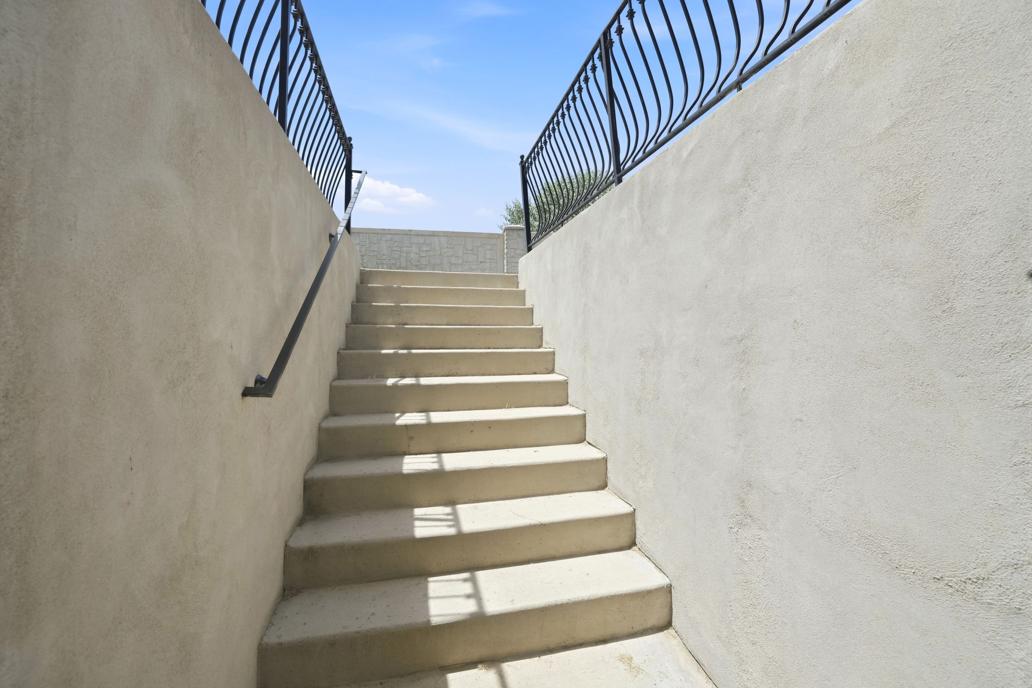Concrete exterior staircase featuring stucco walls and wrought iron railings