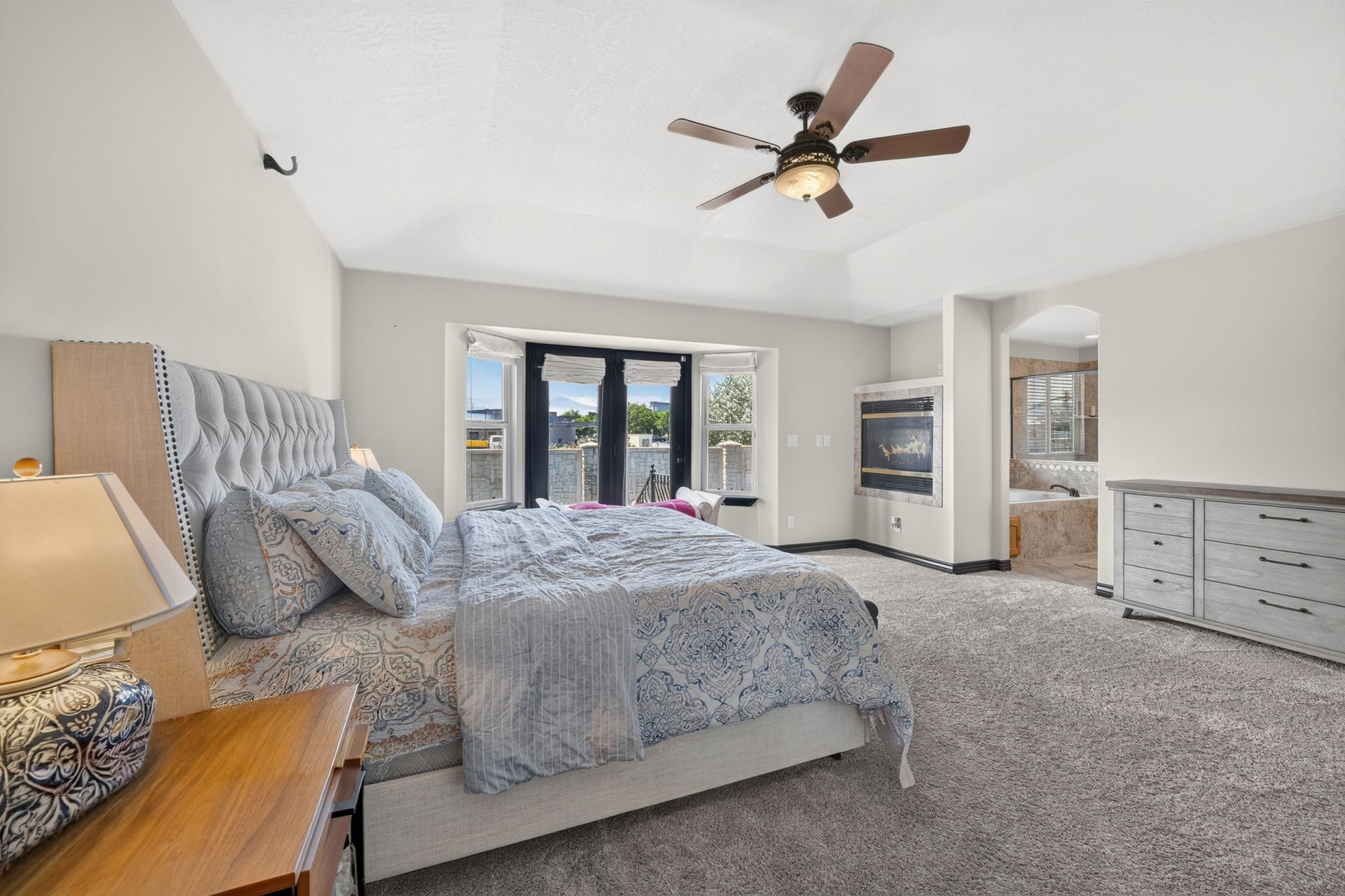 Primary bedroom with Tray ceiling bedroom featuring a ceiling fan, recessed wrap around fireplace, and french doors & bay window with water views