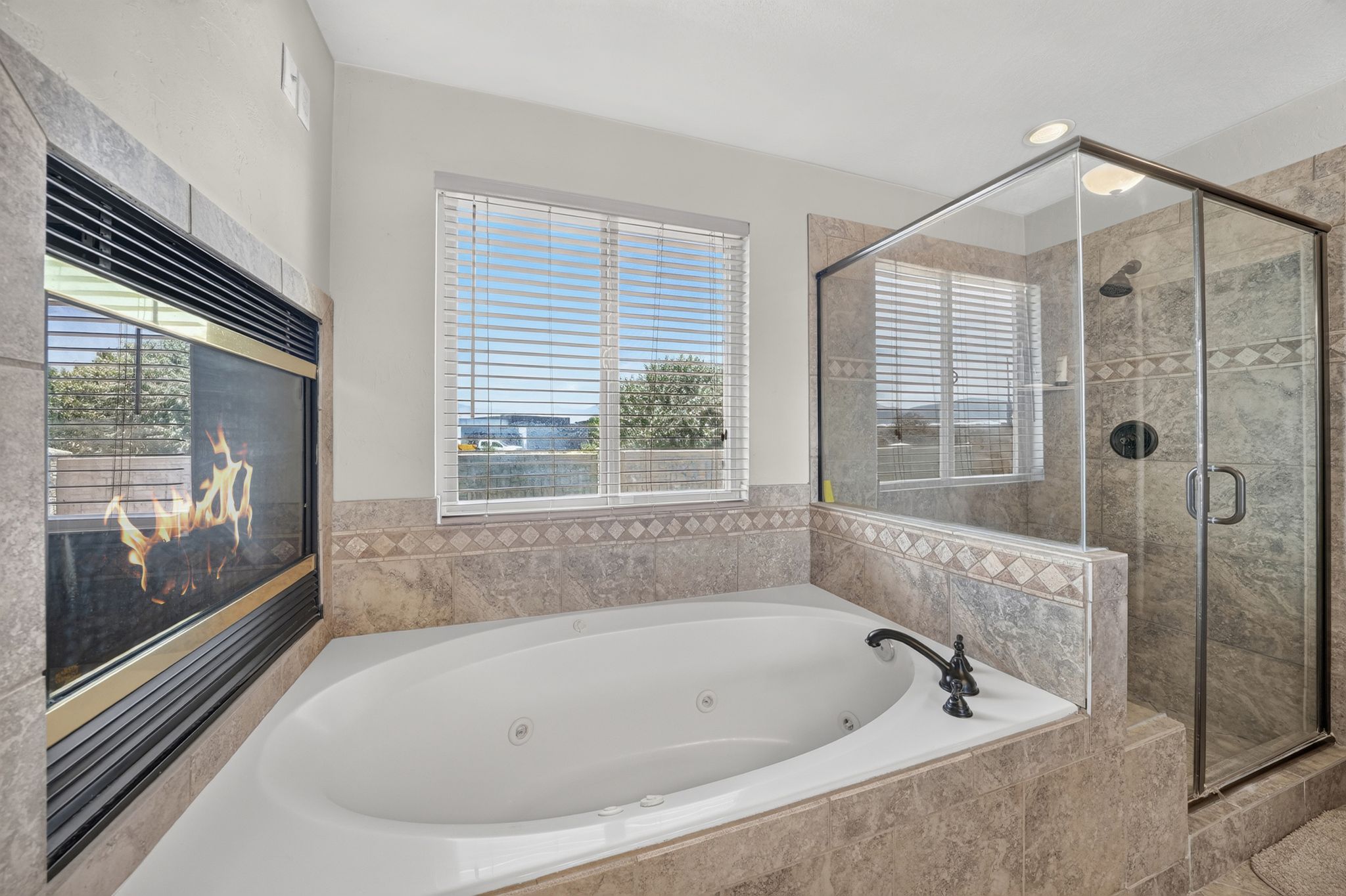 Primary Bathroom Jetted corner tub featuring a dark bronze faucet, a tiled surround, and an adjacent glass-enclosed shower with a rainfall showerhead