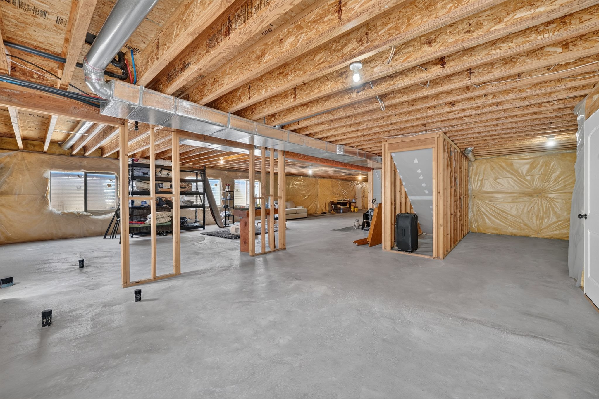 Unfinished basement featuring exposed wood joists, concrete flooring, framed interior walls, and visible ductwork