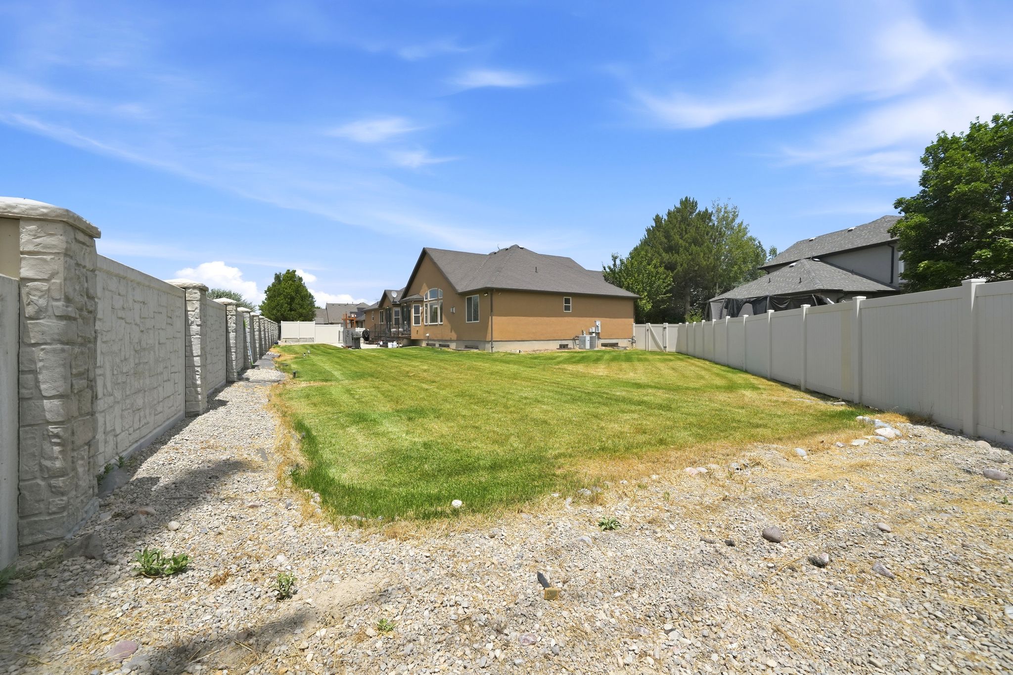 Spacious outdoor area featuring a manicured lawn, stone-finish privacy fencing, and a vinyl privacy fence