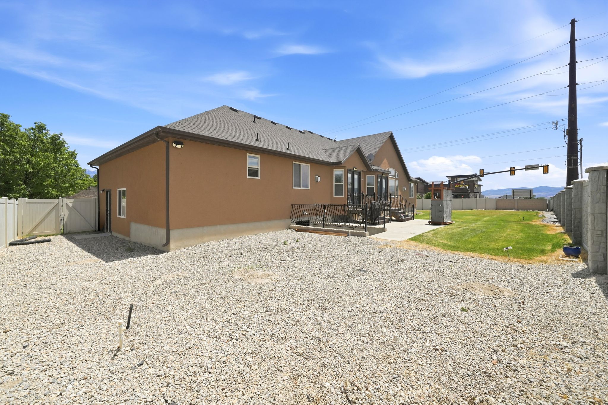 Rear exterior featuring a brown stucco finish, a composite deck, a concrete patio, a gravel area, and a partial grass lawn
