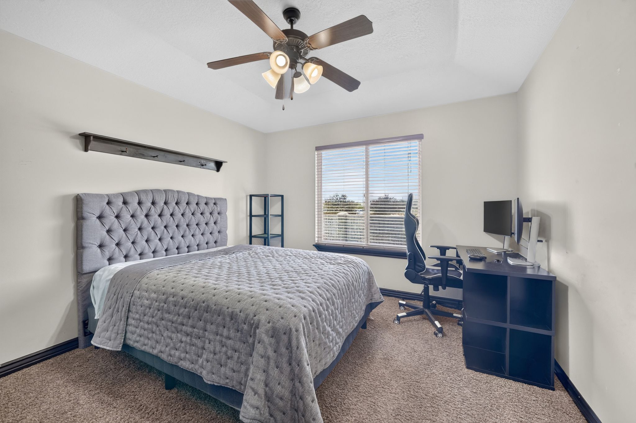 Carpeted Third room featuring a ceiling fan with integrated lighting, a window with horizontal blinds, and a dark wood shelf with hooks