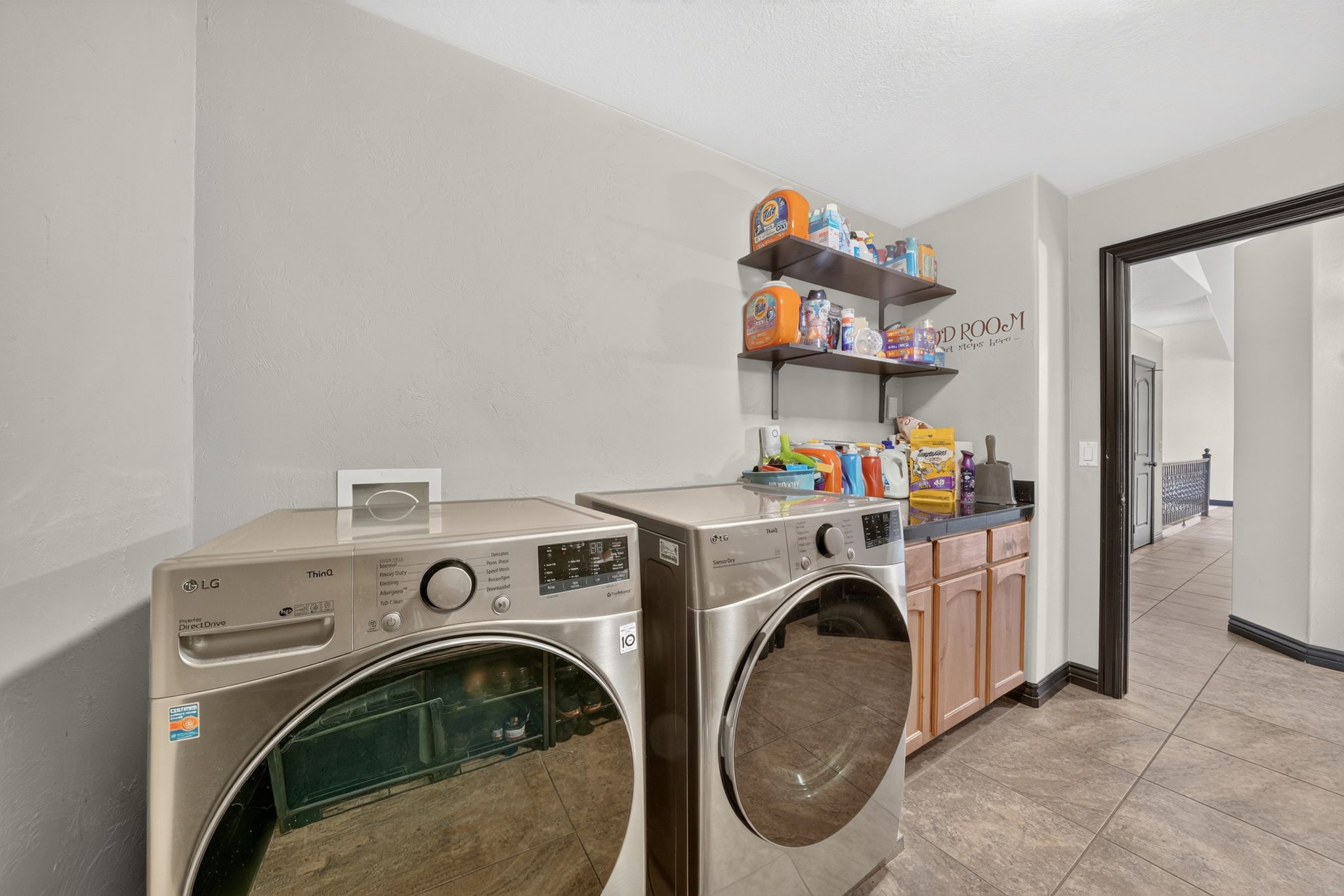 Functional laundry area featuring neutral wall paint, tile flooring, built-in cabinetry with a dark countertop, and two floating shelves