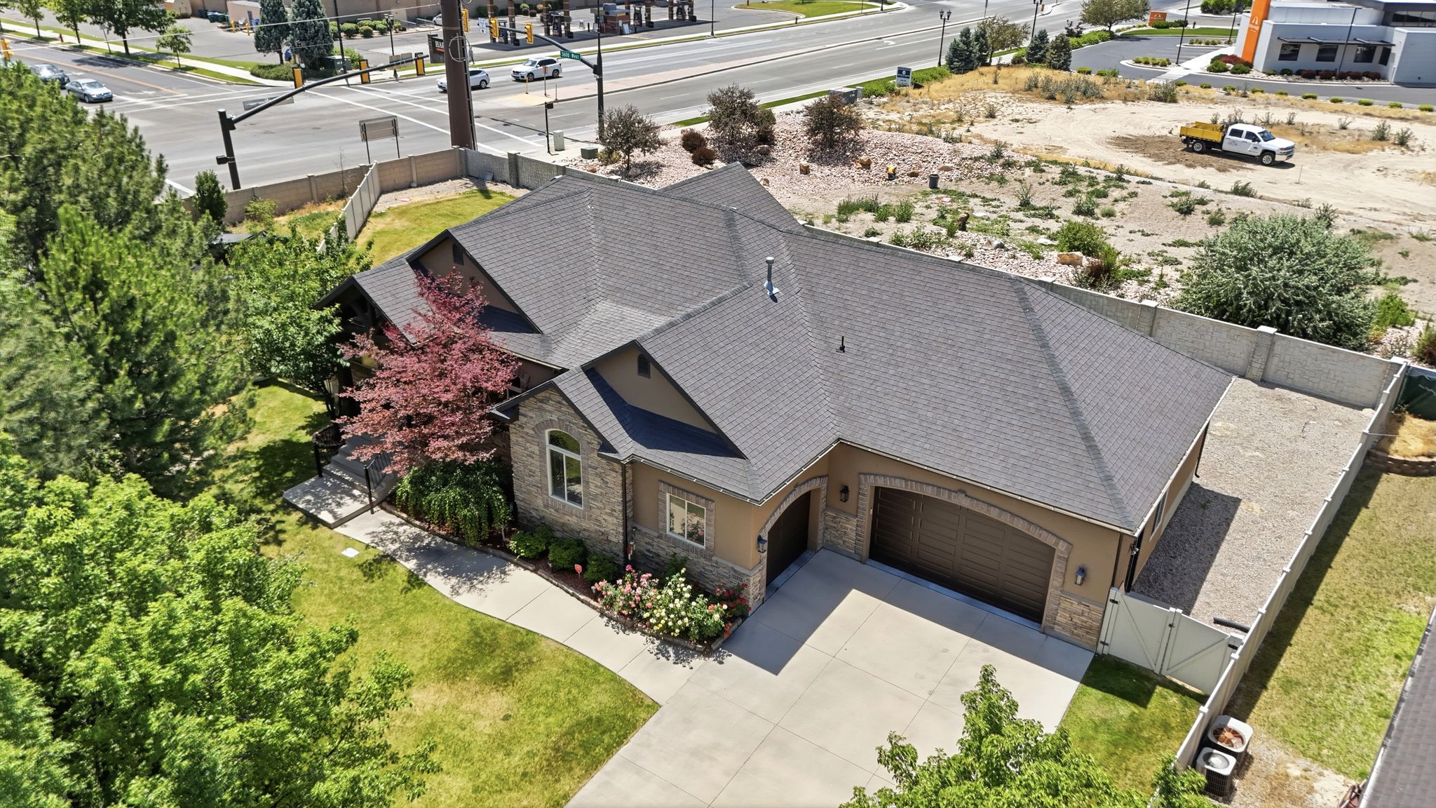 Stucco and stone exterior featuring a dark asphalt shingle roof, arched garage doors, a concrete driveway, and mature landscaping