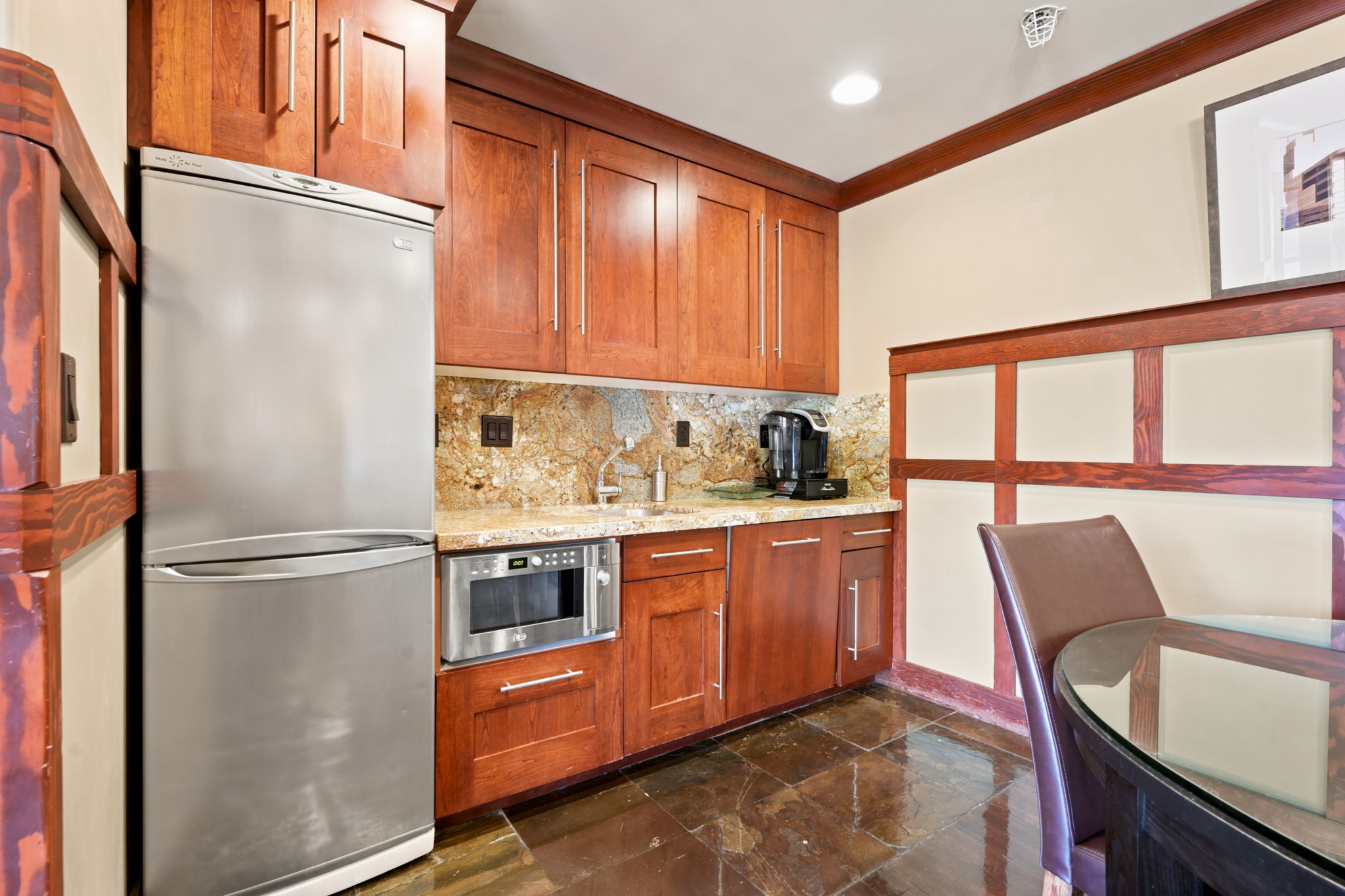 Kitchenette with rich wood-finish cabinetry, granite backsplash, and coordinating countertop