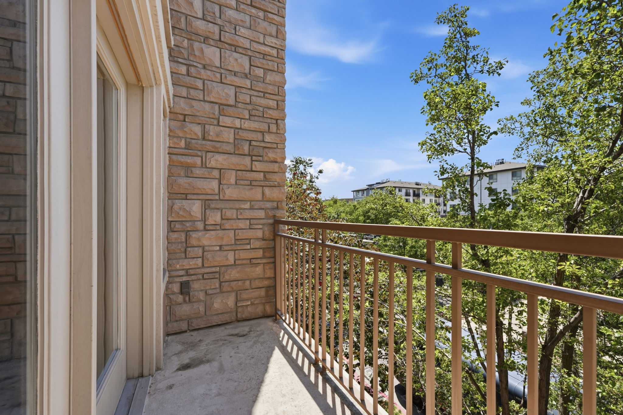 Private balcony featuring a stone veneer exterior, a metal railing, and a concrete floor