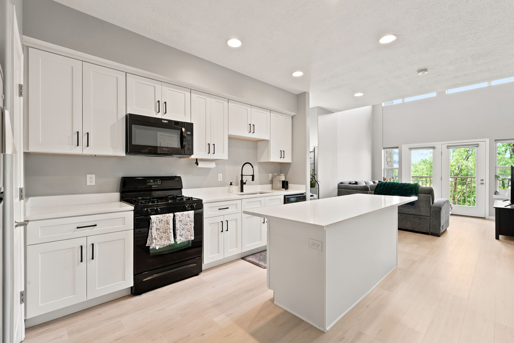 Contemporary kitchen featuring white cabinetry, black hardware, a black range with an overhead microwave, and a central island with a solid surface countertop