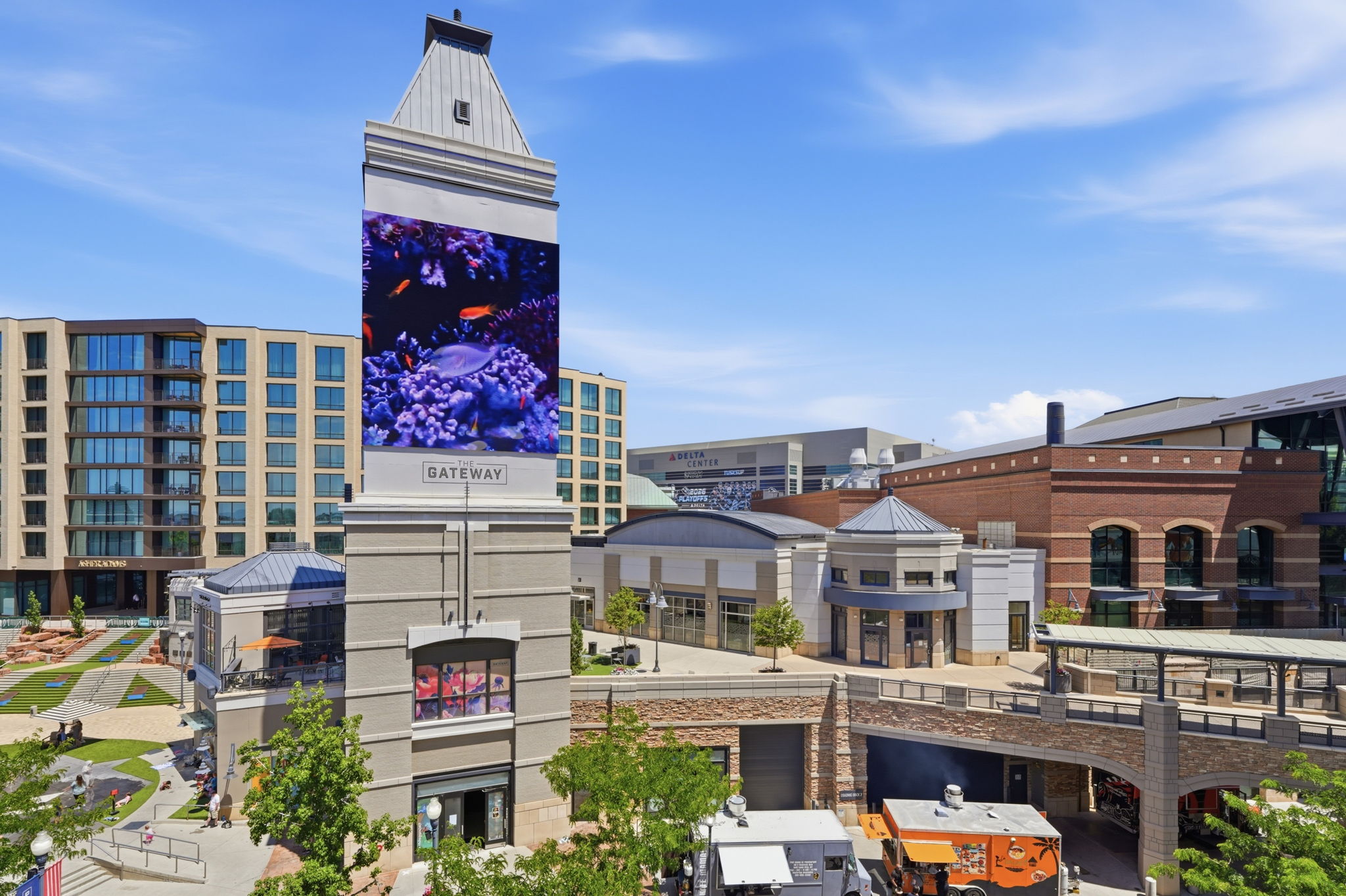 Modern urban development featuring a prominent tower with a large digital display, multi-story residential buildings, and commercial spaces with retail storefronts