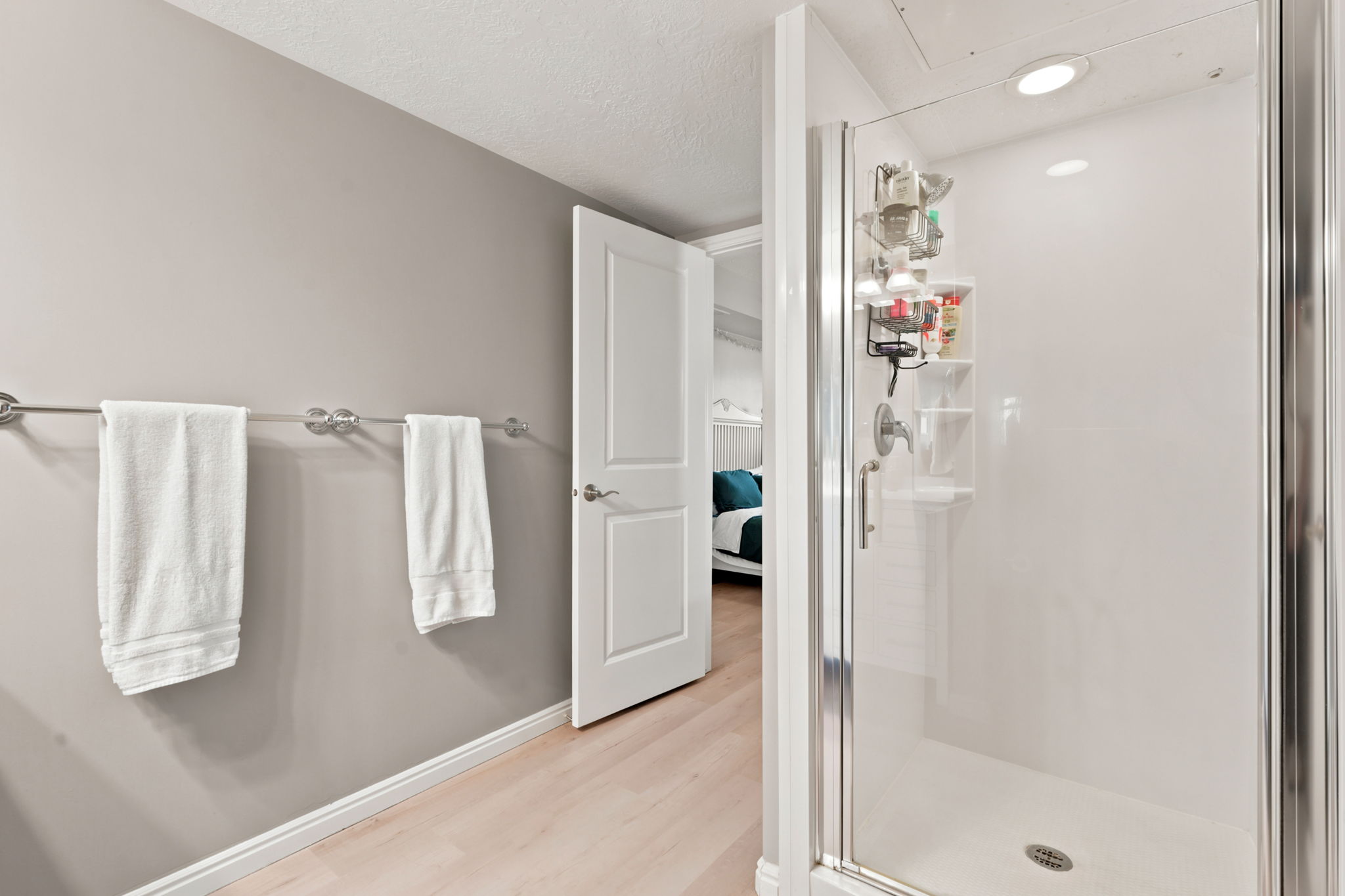 Walk-in shower with clear glass door, chrome fixtures, recessed lighting, and light wood-finish flooring