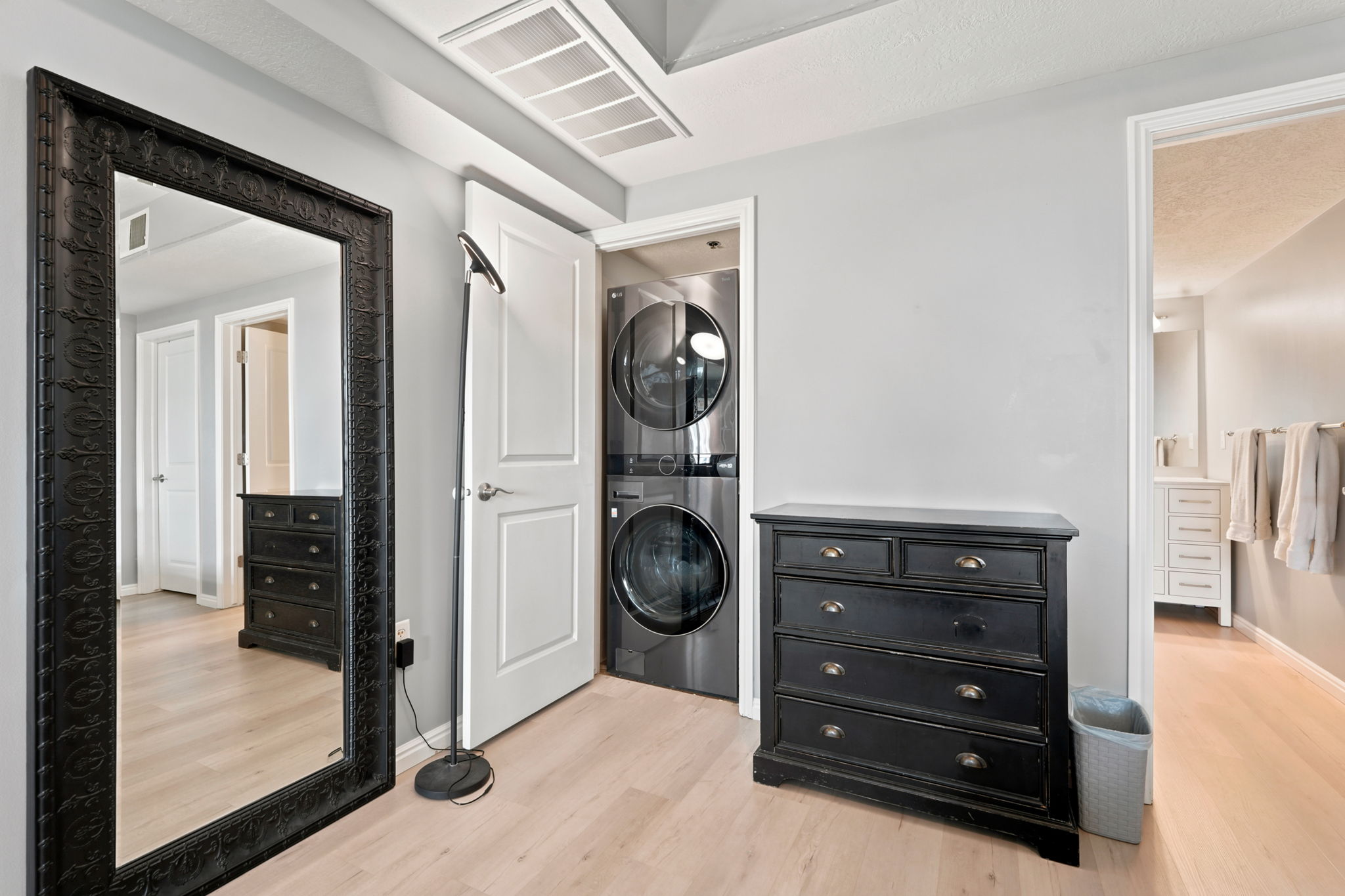 Stackable washer and dryer unit, light wood-finish flooring, and a ceiling vent
