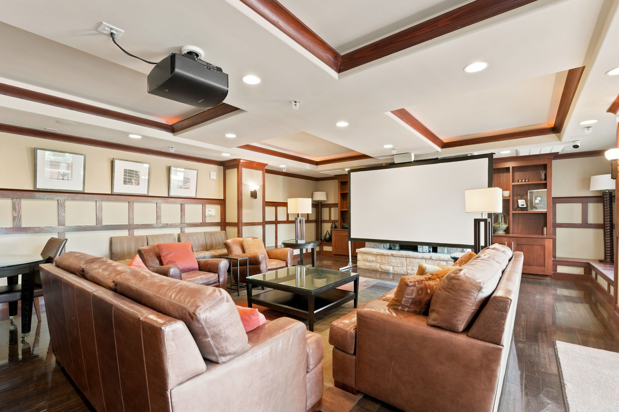 Entertainment room featuring a ceiling-mounted projector, retractable screen, tray ceiling with recessed lighting, dark wood-finish flooring, and built-in shelving