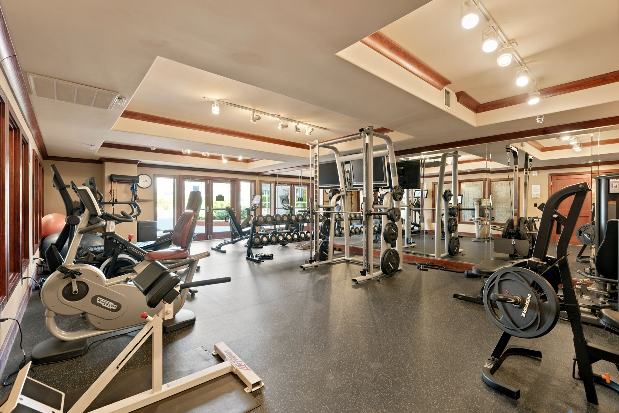 Dedicated fitness center featuring rubber flooring, mirrored wall, recessed and track lighting, wood-trimmed ceiling, and multiple windowed doors
