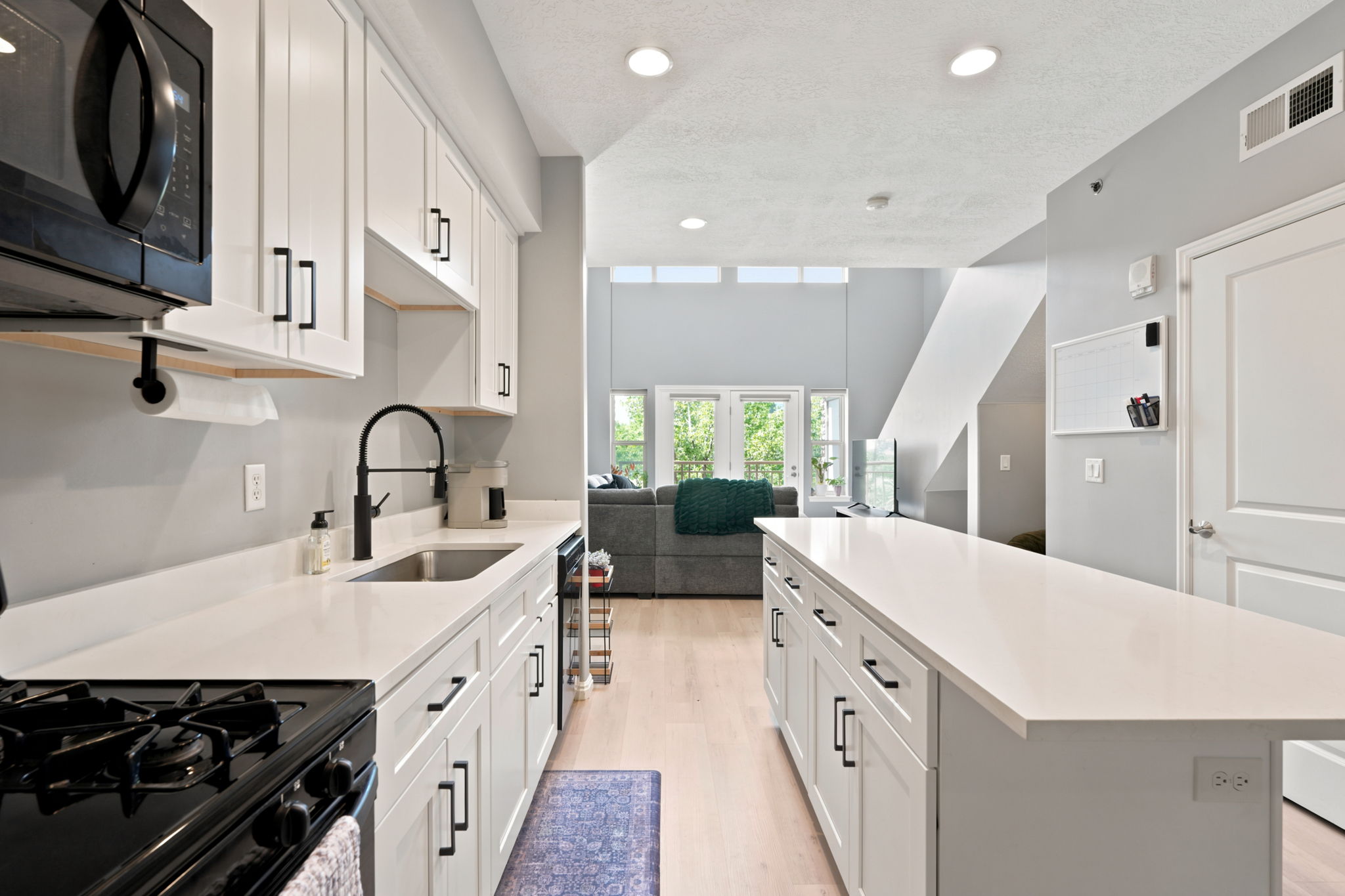 Kitchen featuring white shaker cabinetry, white countertops, a stainless steel sink with a matte black faucet, and wood-finish flooring