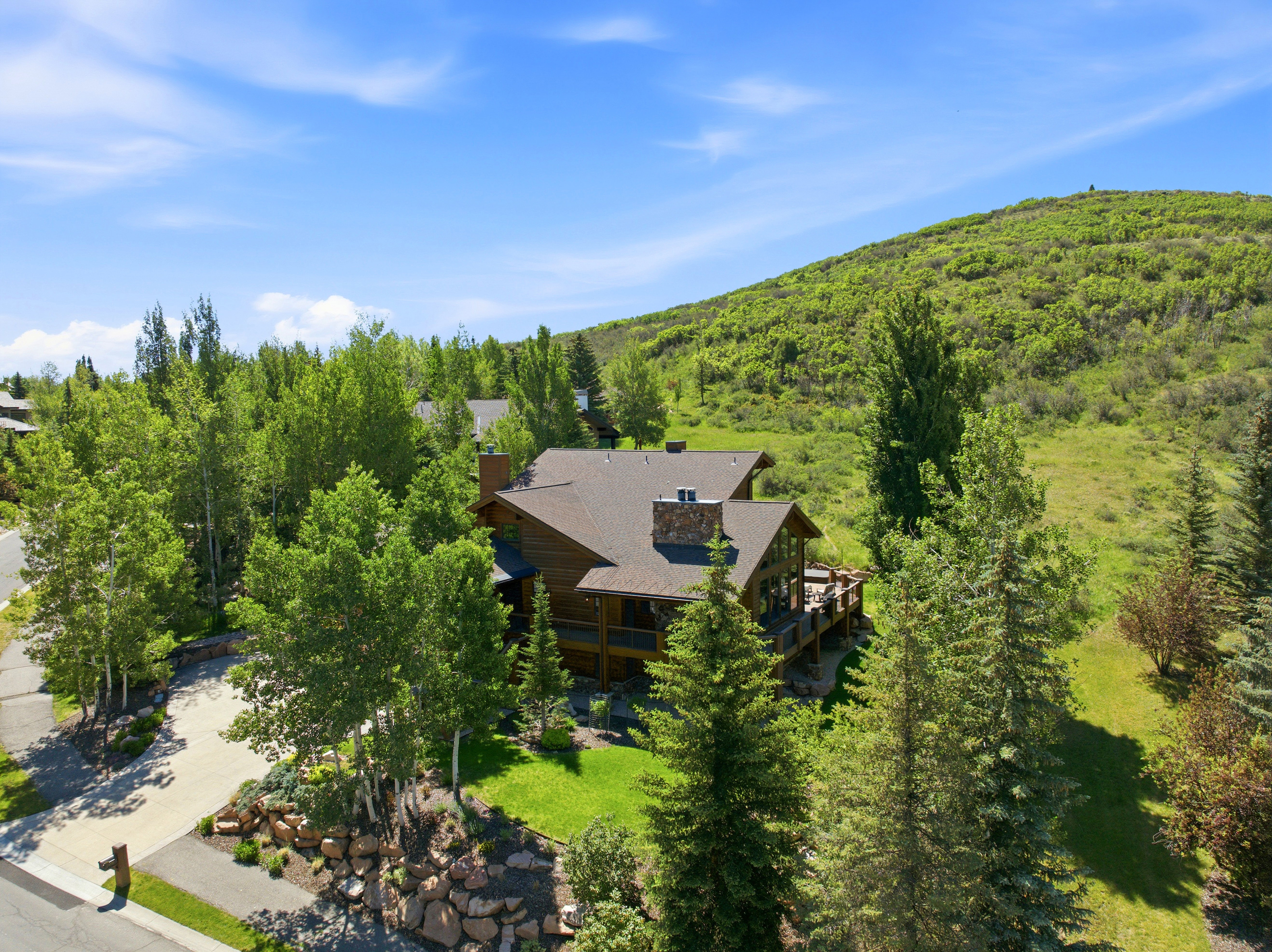 Wood-sided residence with multiple outdoor deck areas, a prominent stone chimney, and a brown shingle roof