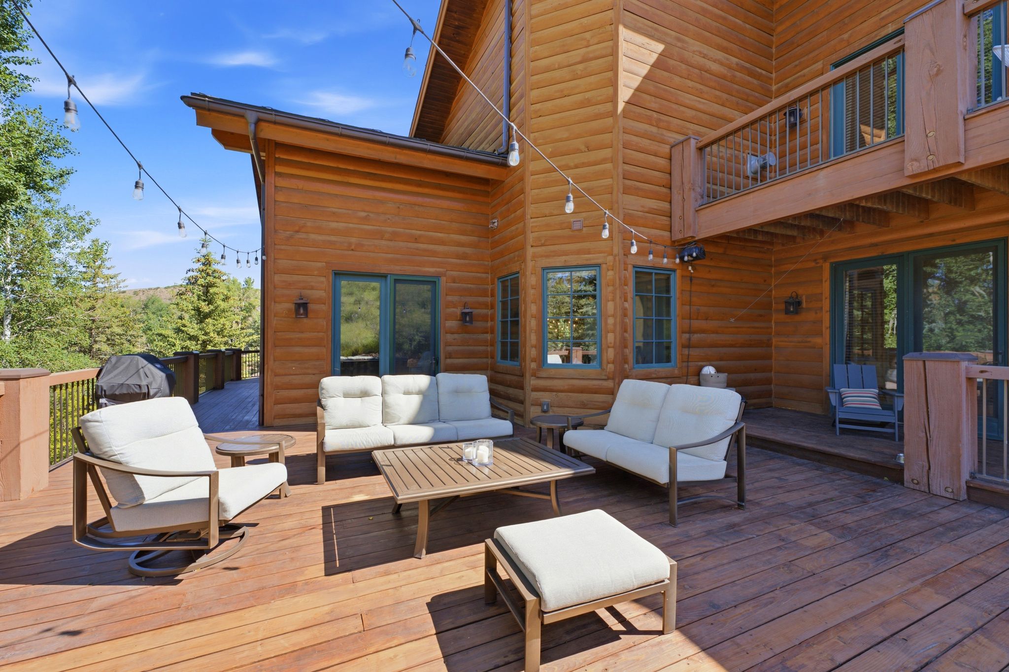 Expansive multi-level wood deck featuring a log cabin exterior, string lighting, and direct outdoor access