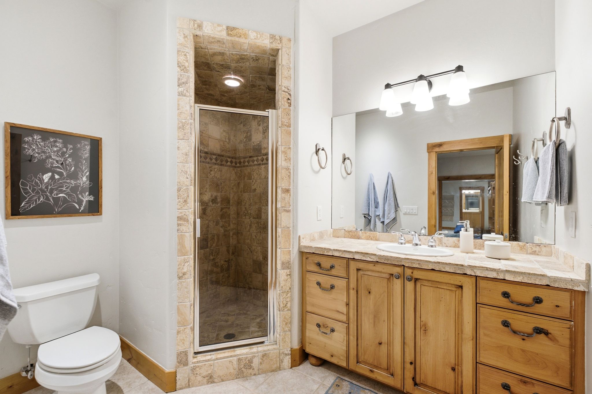 Bathroom featuring a glass-enclosed shower with stone tile surround, a built-in wood vanity with an undermount sink, a stone countertop, and a wall-mounted light fixture