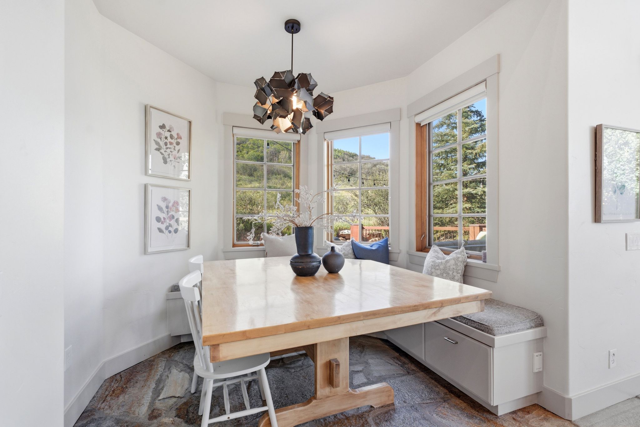 Corner dining nook featuring large windows, stone-finish flooring, a built-in bench with storage, and a contemporary chandelier