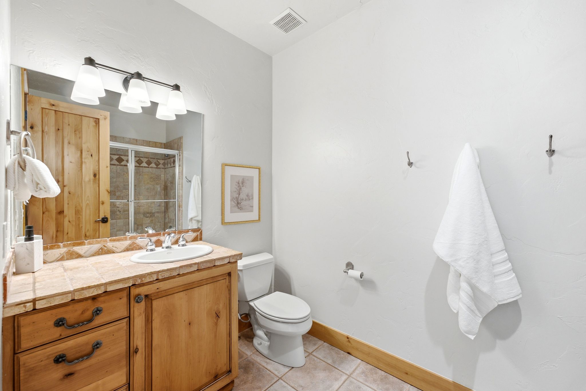 Bathroom featuring a tiled vanity with integrated sink, wood-finish cabinetry, and a full-width mirror with overhead lighting