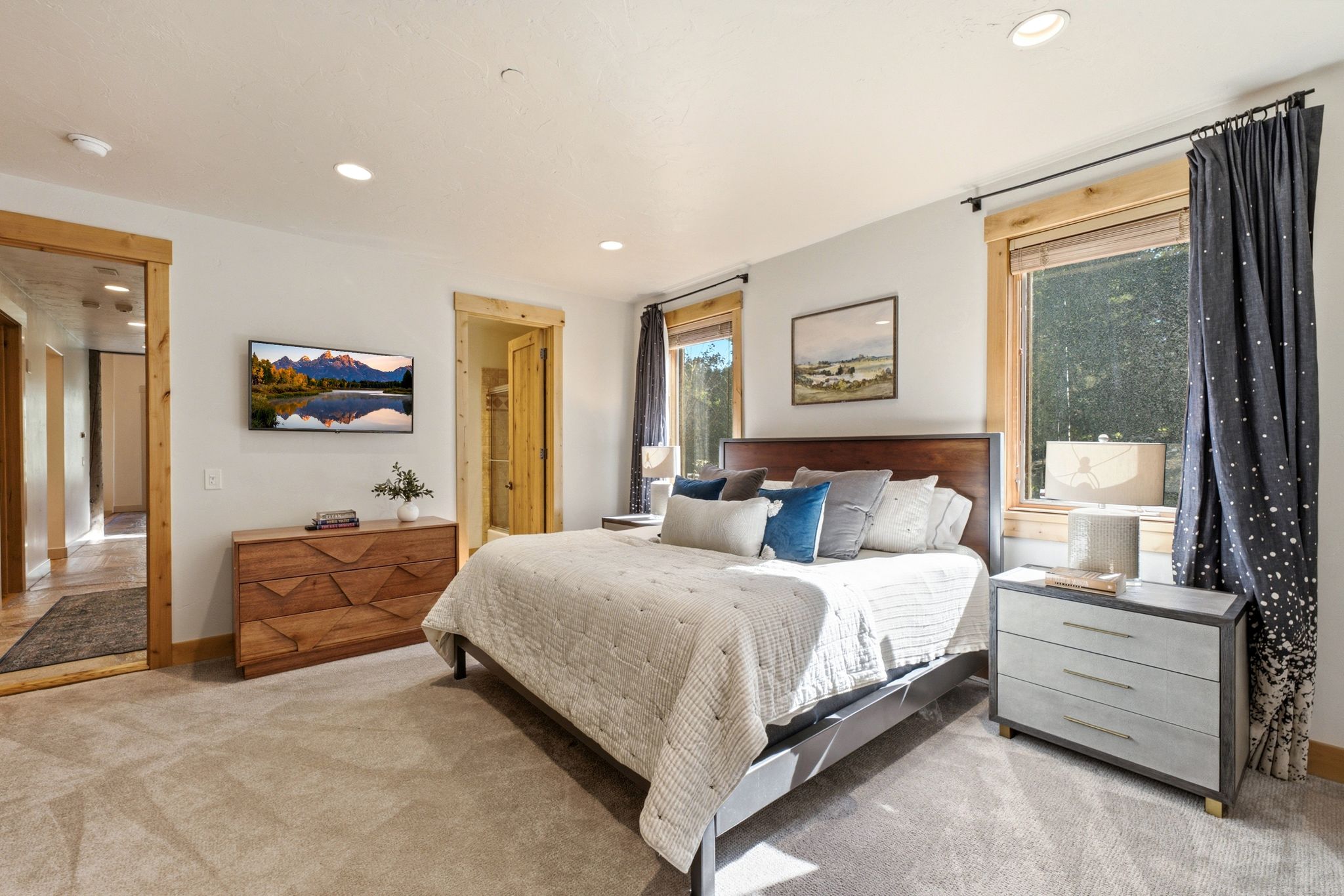 Light-toned carpeting enhances this sleeping area featuring two windows with natural wood trim