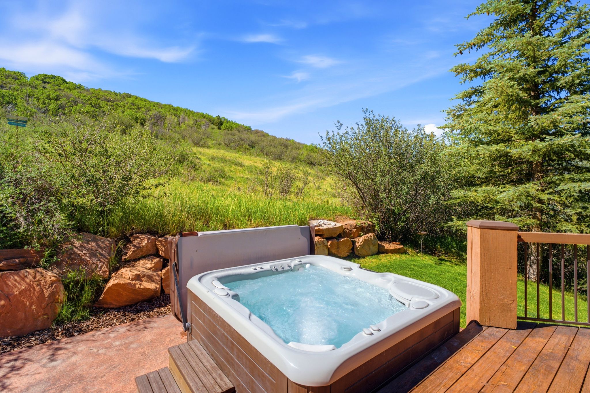 Outdoor hot tub with integrated steps on a concrete patio, bordered by a wooden deck with black metal railings