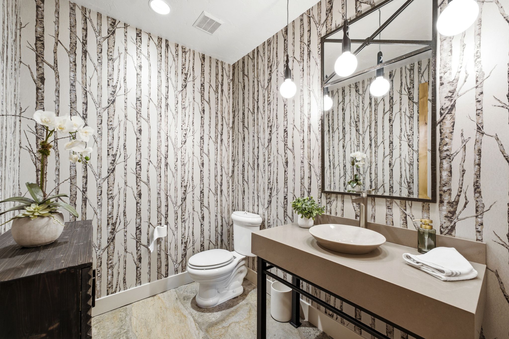 Powder room featuring tree-patterned wallpaper, a vessel sink with wall-mounted faucet, and a large framed mirror with integrated spherical lighting