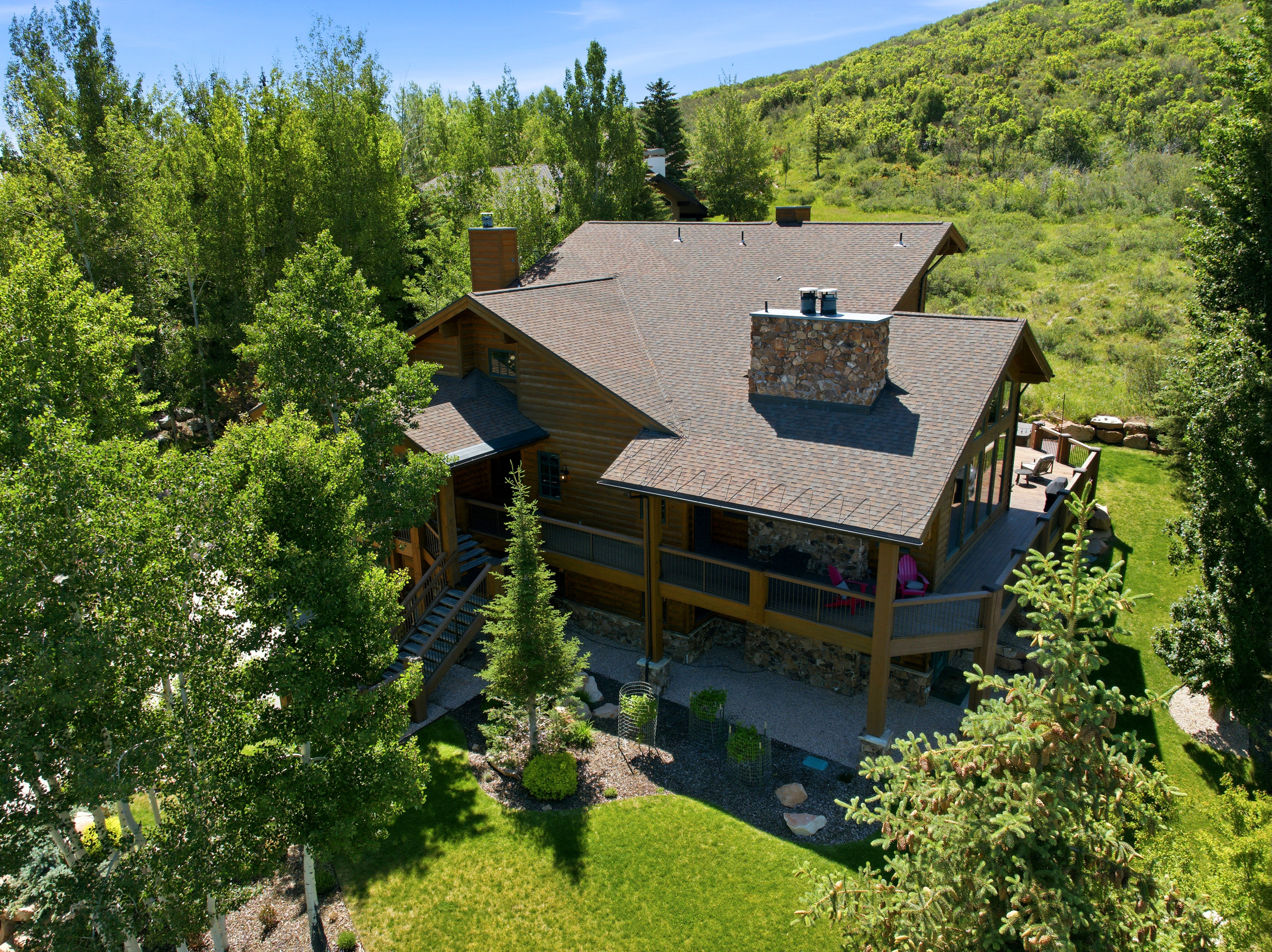Wood-sided residence featuring a multi-level deck, stone chimney, and a multi-pitch shingle roof