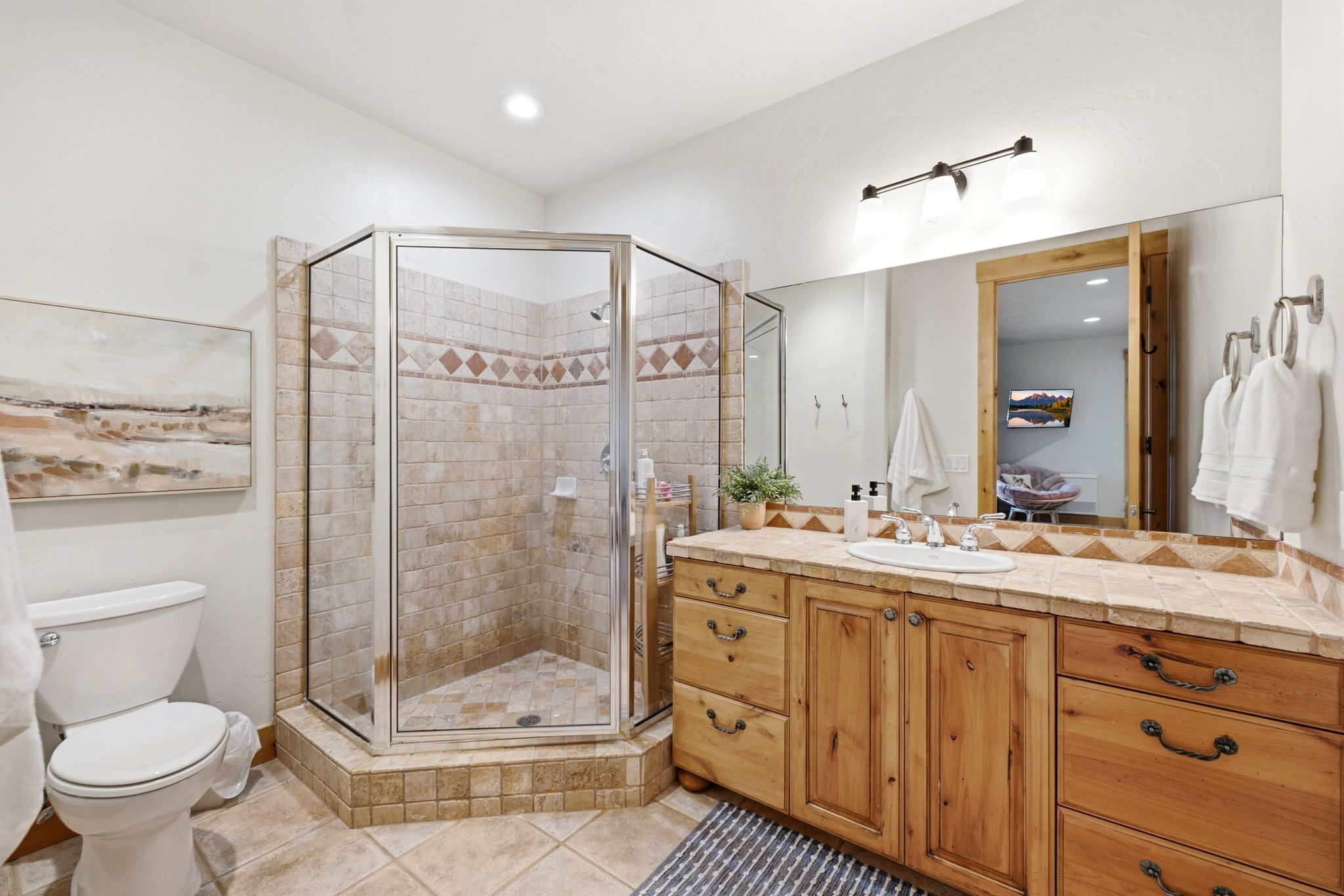 Tile-surround shower with glass enclosure, single vanity with wood cabinetry, and a tile countertop