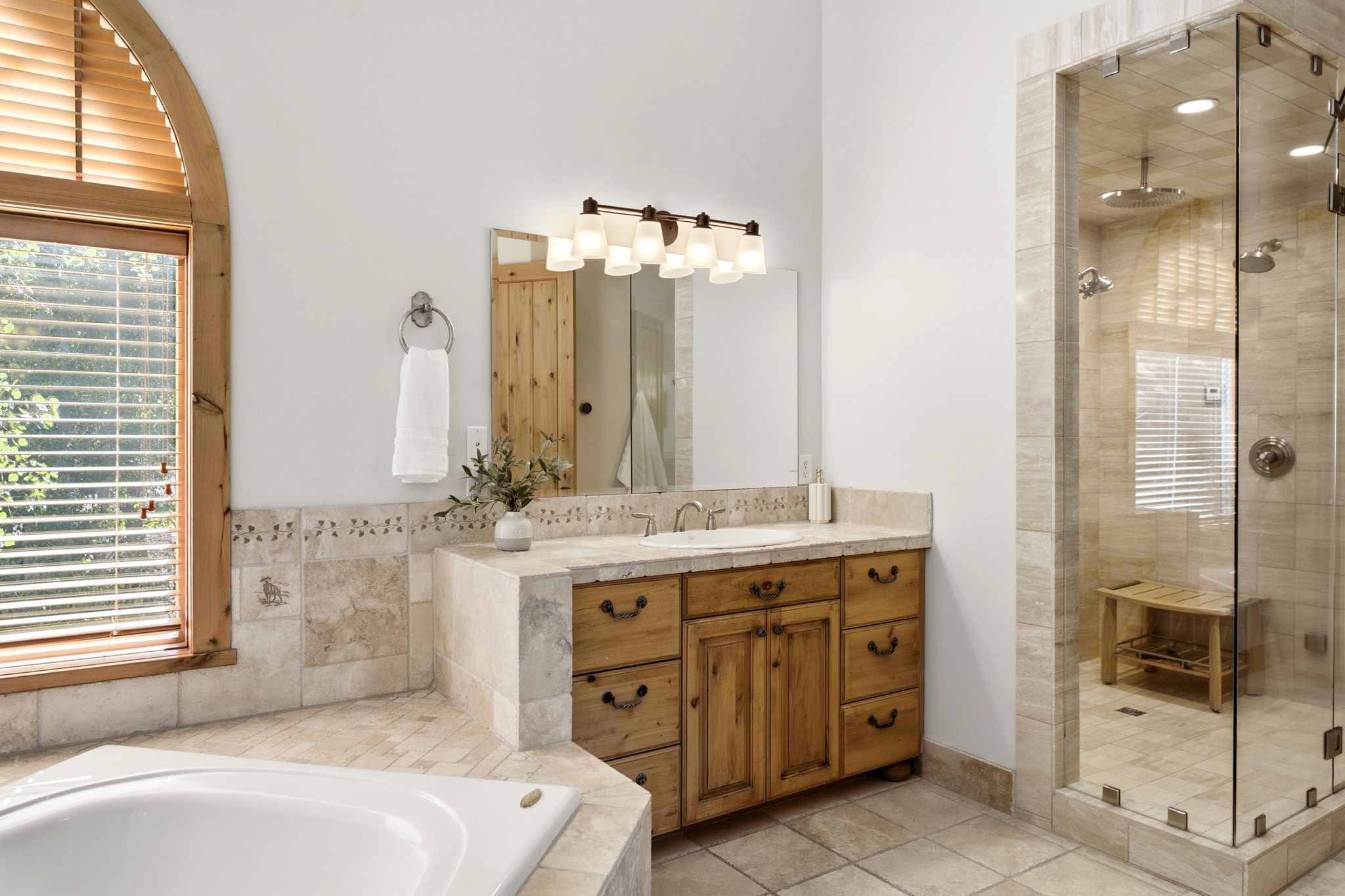 Bathroom featuring a glass-enclosed shower, a corner built-in bathtub, a wood-finish vanity with a stone-finish countertop, and an arched window with wood-finish trim