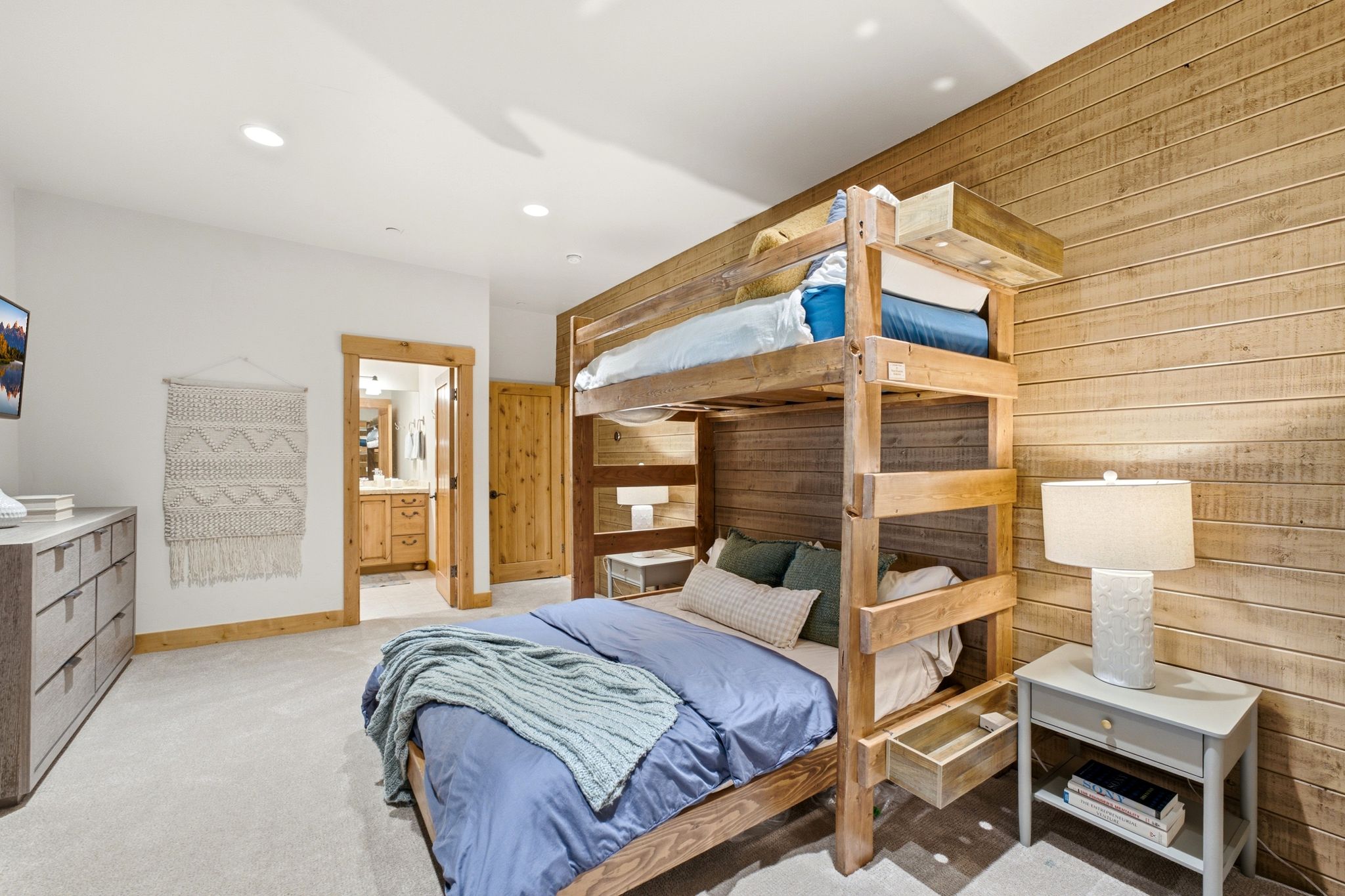 Wood-paneled accent wall in a carpeted room featuring a built-in bunk bed with integrated storage