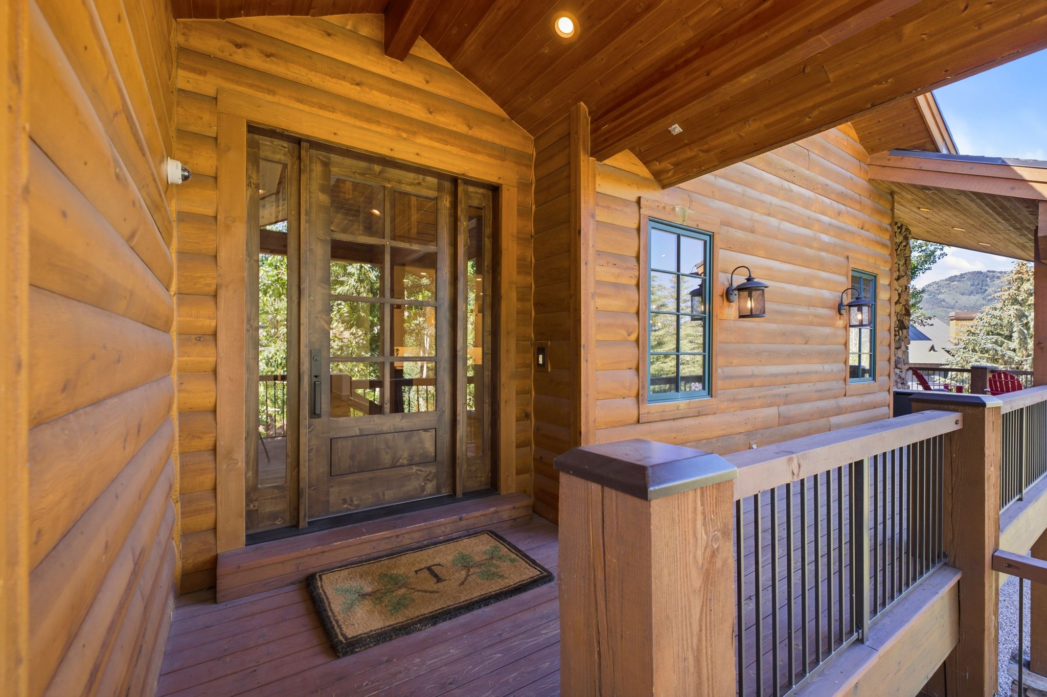 Wood-sided exterior featuring a glass-paned entry door with sidelights, a covered porch with wood railings and black vertical balusters, and wall-mounted exterior light fixtures