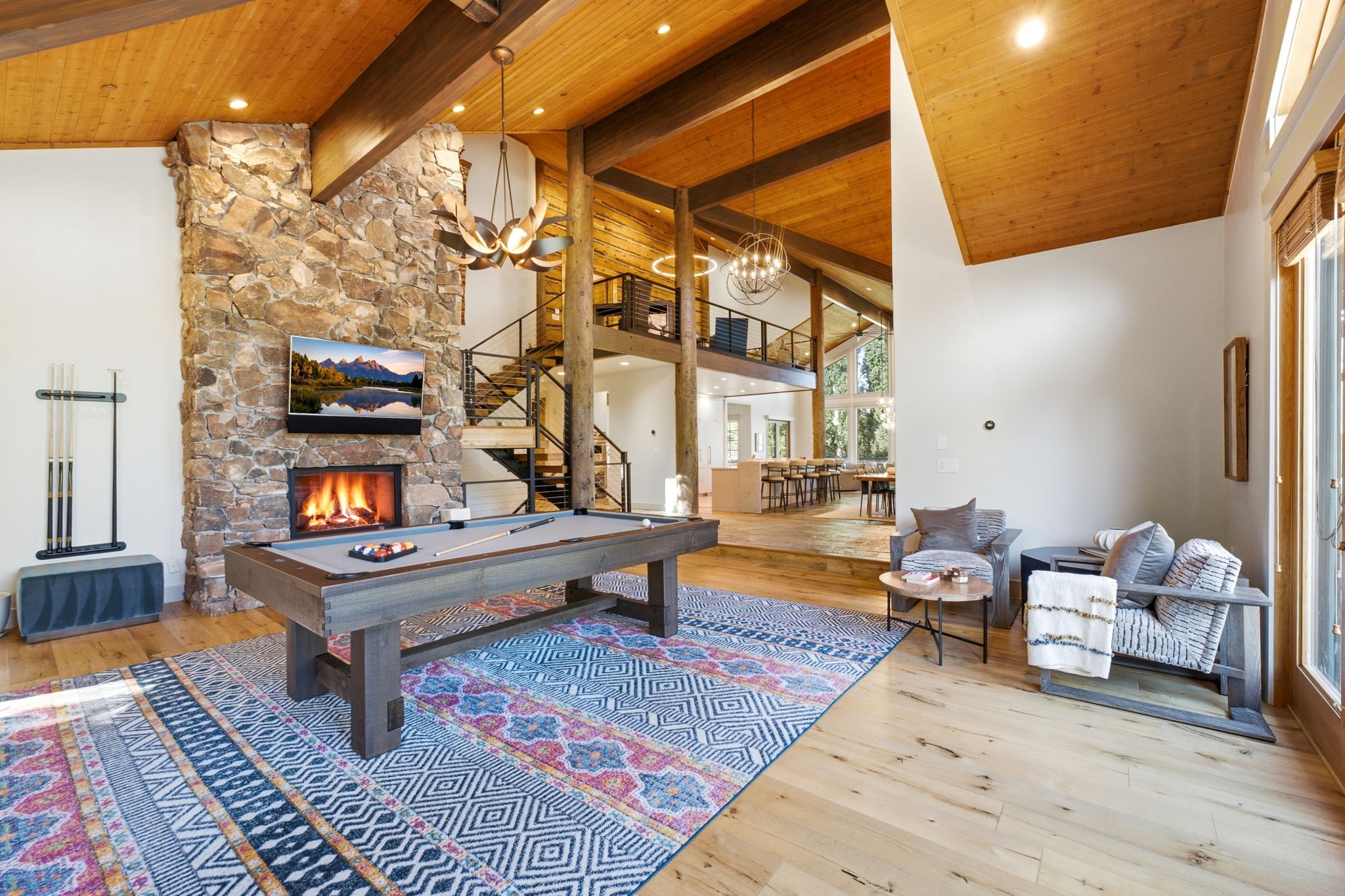 Spacious living area featuring a floor-to-ceiling stone fireplace with an integrated hearth, vaulted wood-paneled ceilings with exposed beams, wood-finish flooring, and expansive windows