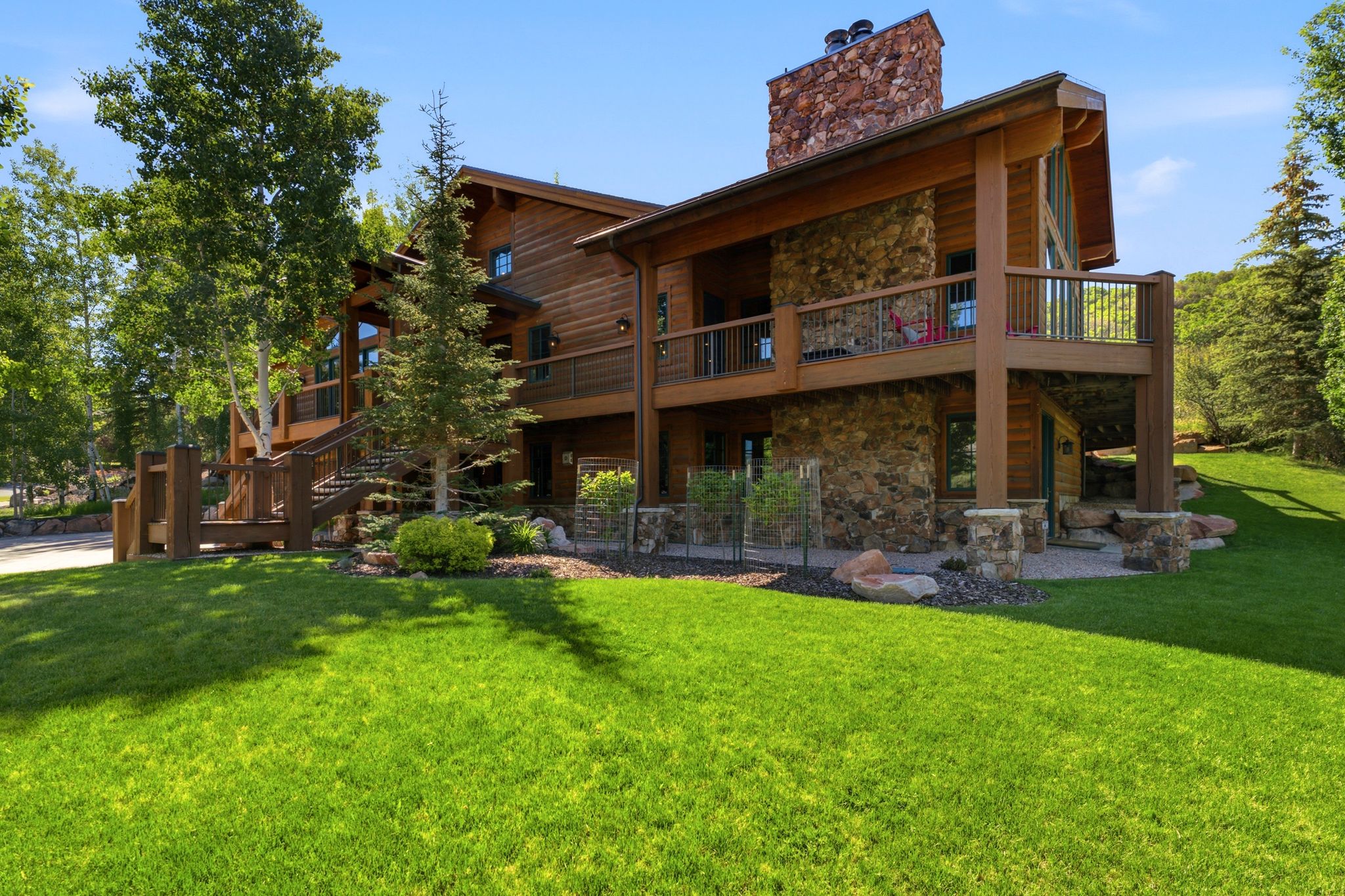 Multi-level rustic residence featuring a prominent stone chimney, wood siding, and an expansive lawn