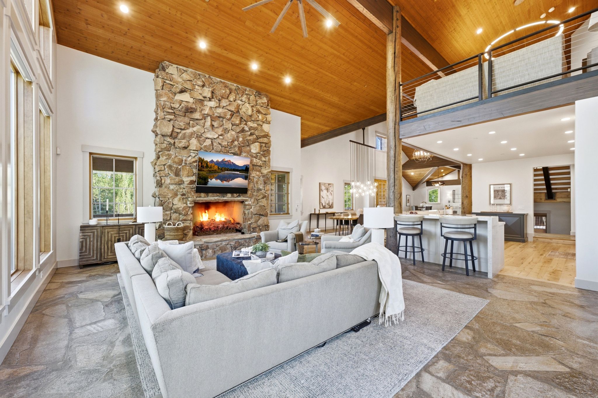 Spacious great room featuring a floor-to-ceiling stone fireplace, vaulted wood-paneled ceiling, and flagstone flooring