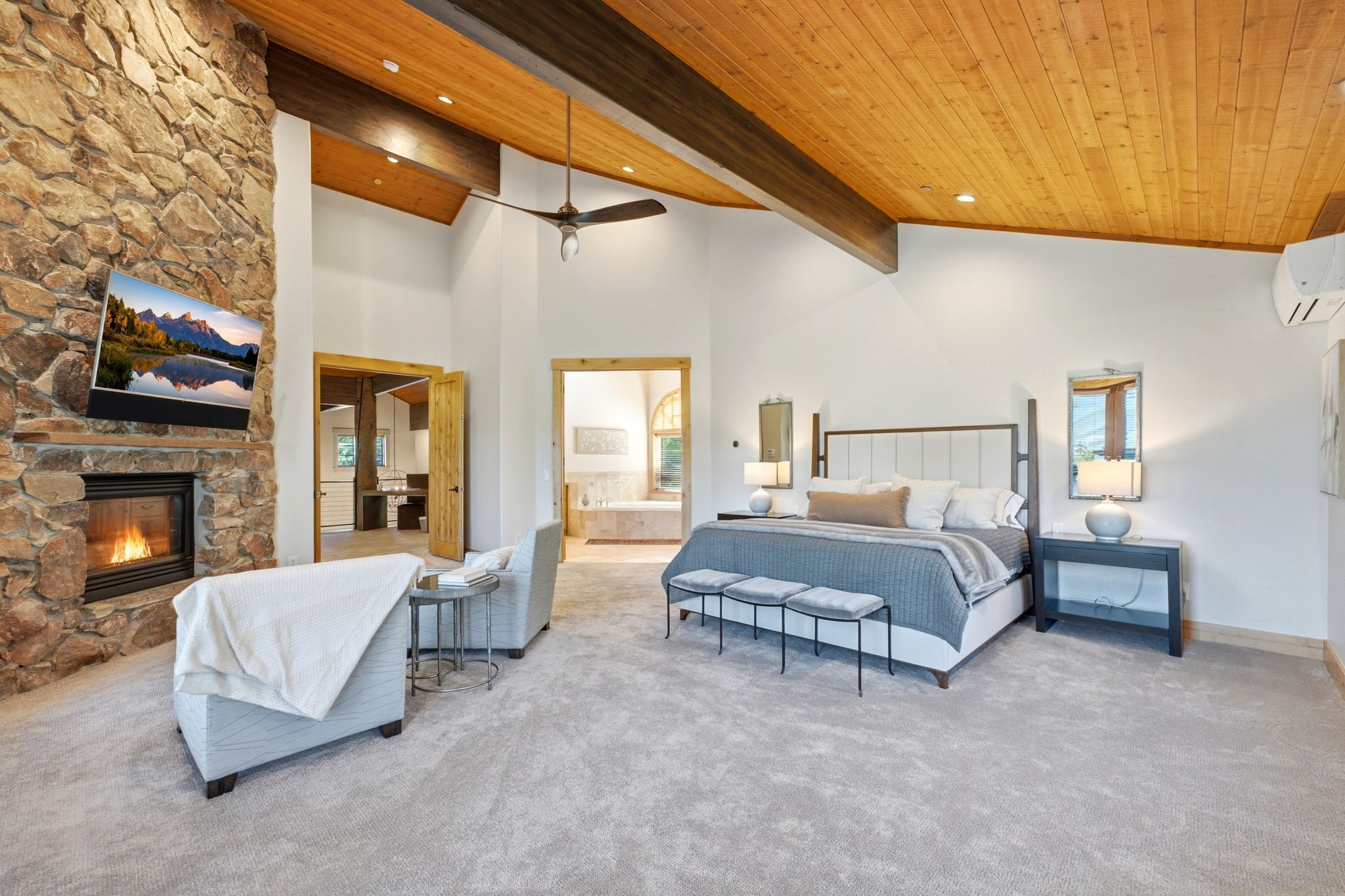 Spacious interior featuring a stone fireplace, vaulted wood-paneled ceiling, exposed wood beams, and neutral carpeting
