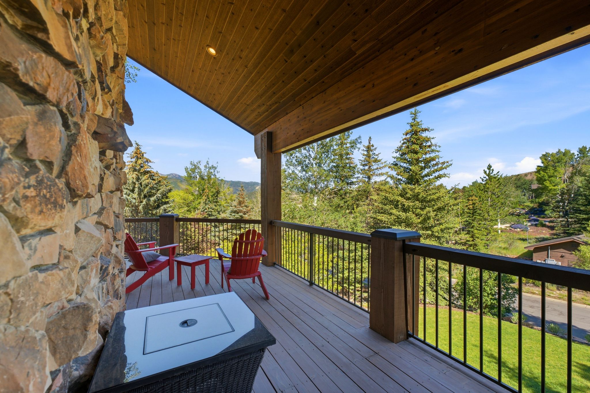 Expansive outdoor deck featuring a stone-clad exterior wall, wood-finish ceiling, durable composite decking, and metal railing