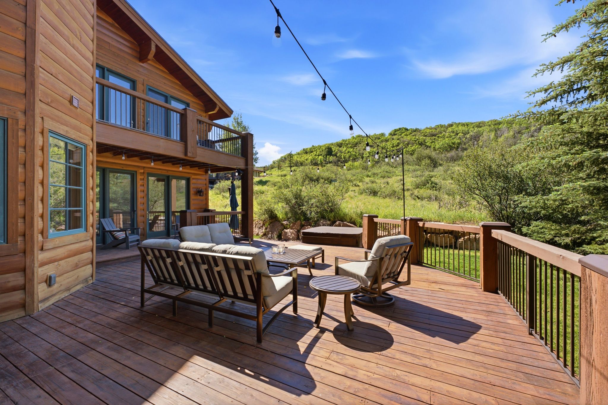 Expansive multi-level wood deck featuring a built-in spa, dark metal railings, and string lighting