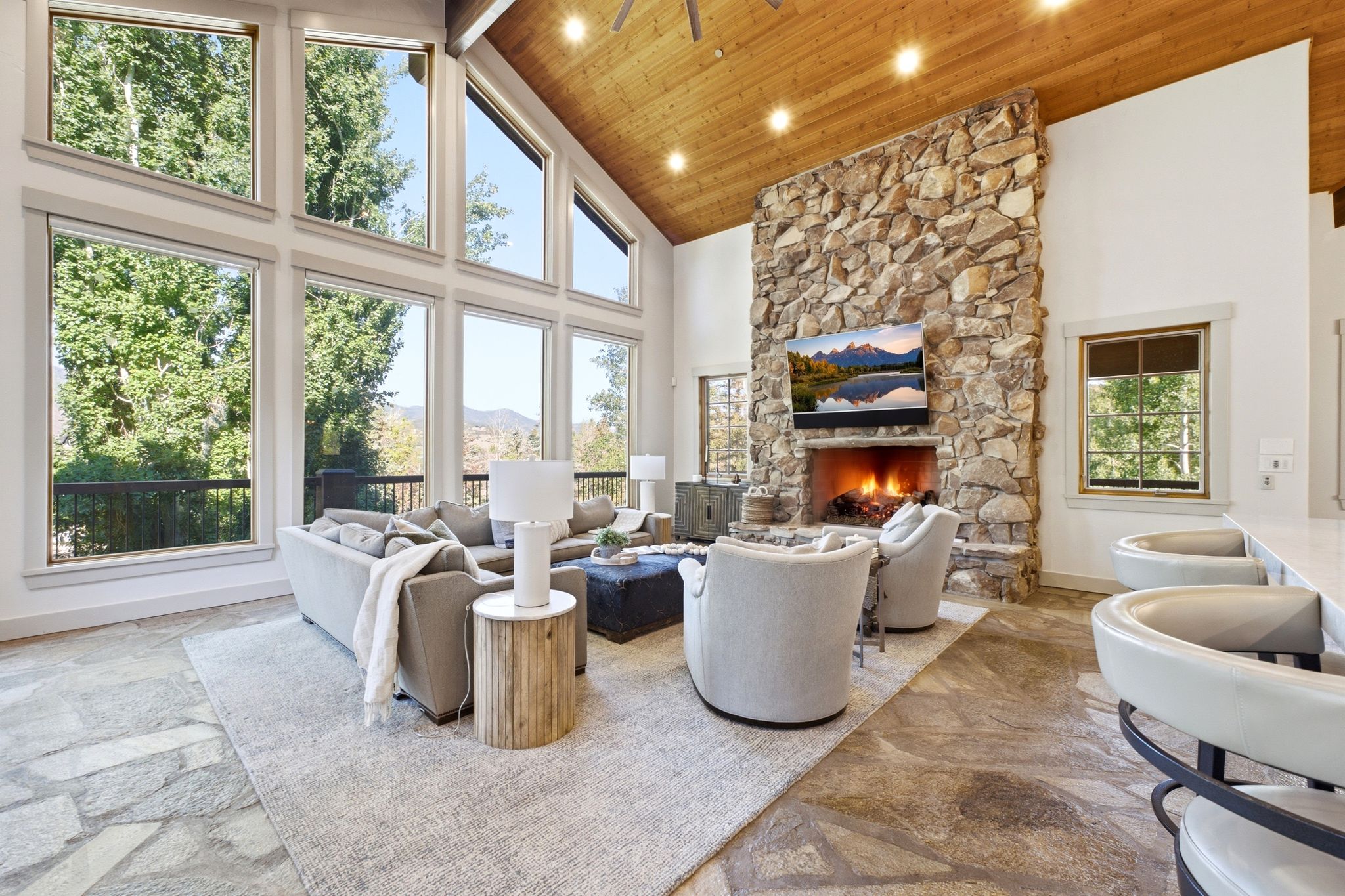 Great room featuring a vaulted wood-paneled ceiling, floor-to-ceiling windows, a stone-clad fireplace, and flagstone flooring