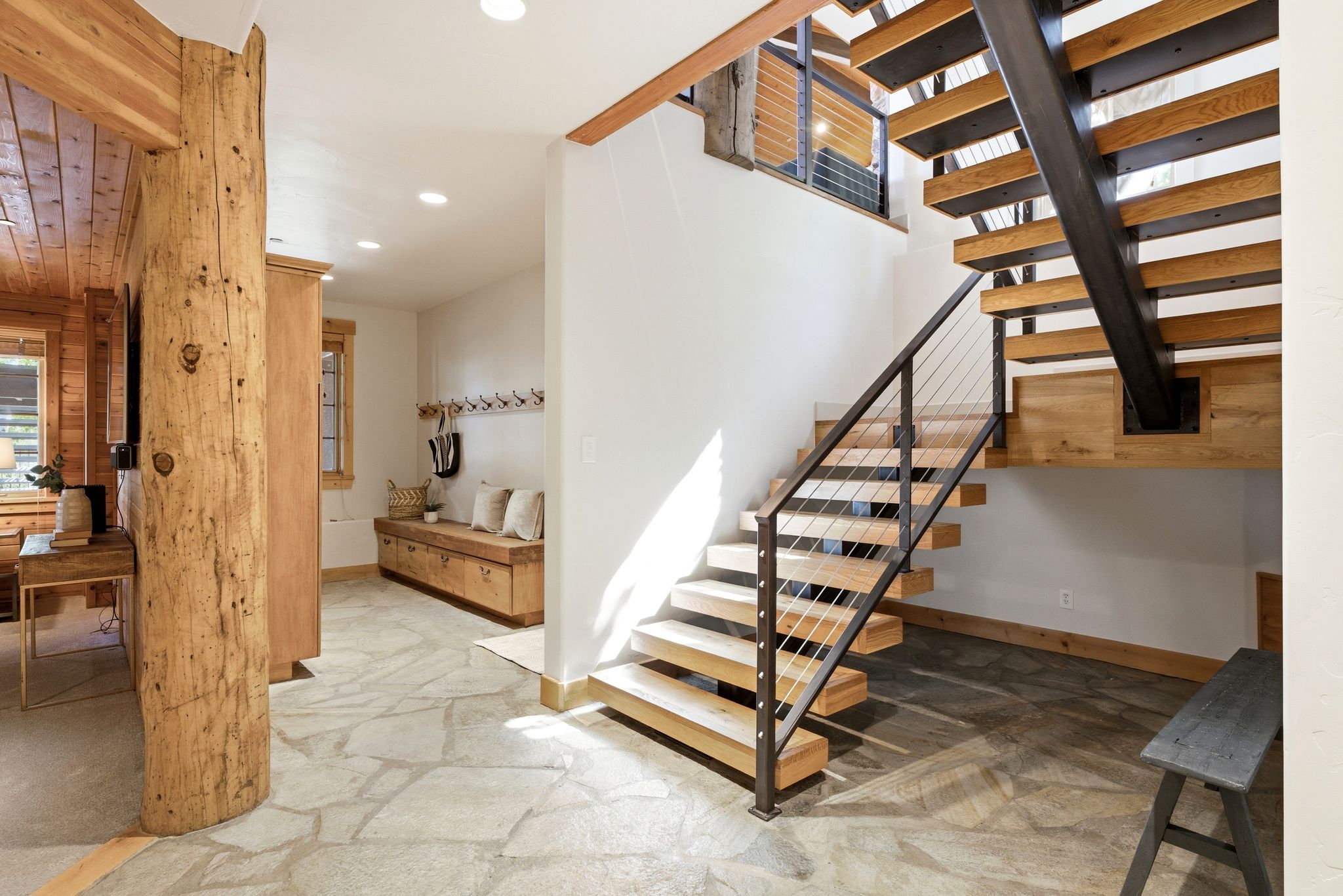 Modern floating staircase with metal and cable railings, natural wood treads, and exposed structural beam