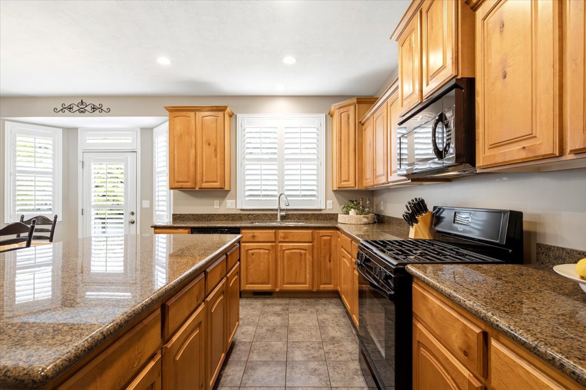 Kitchen featuring wood cabinetry, speckled countertops, stainless steel sink with a gooseneck faucet, black appliances, and tile flooring