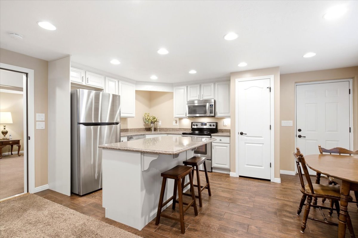 Kitchen featuring a center island with countertop seating, stainless steel appliances, white cabinetry, and wood-finish flooring