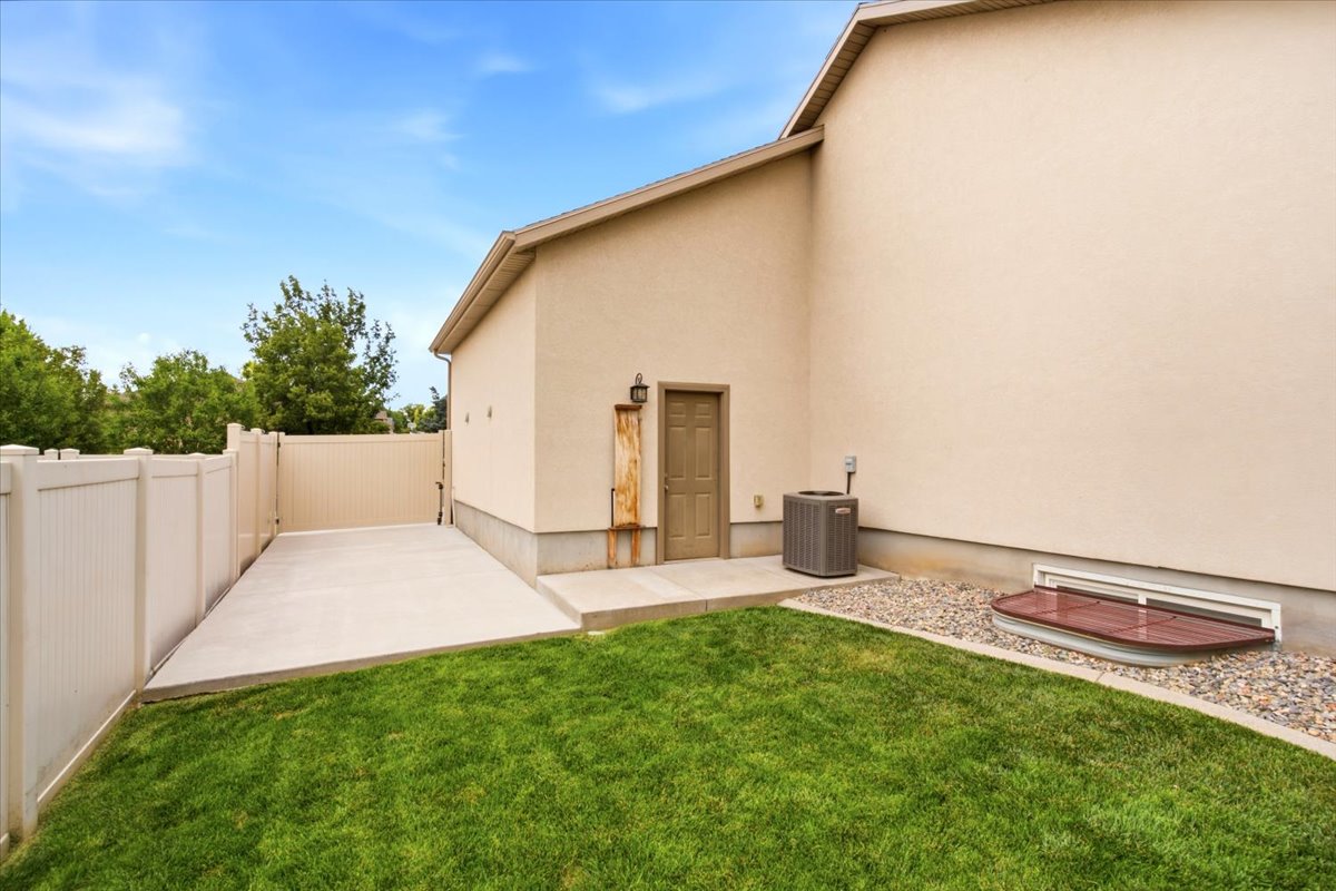 Rear exterior featuring a manicured lawn, gravel landscaping, a window well, and a concrete patio with an exterior door